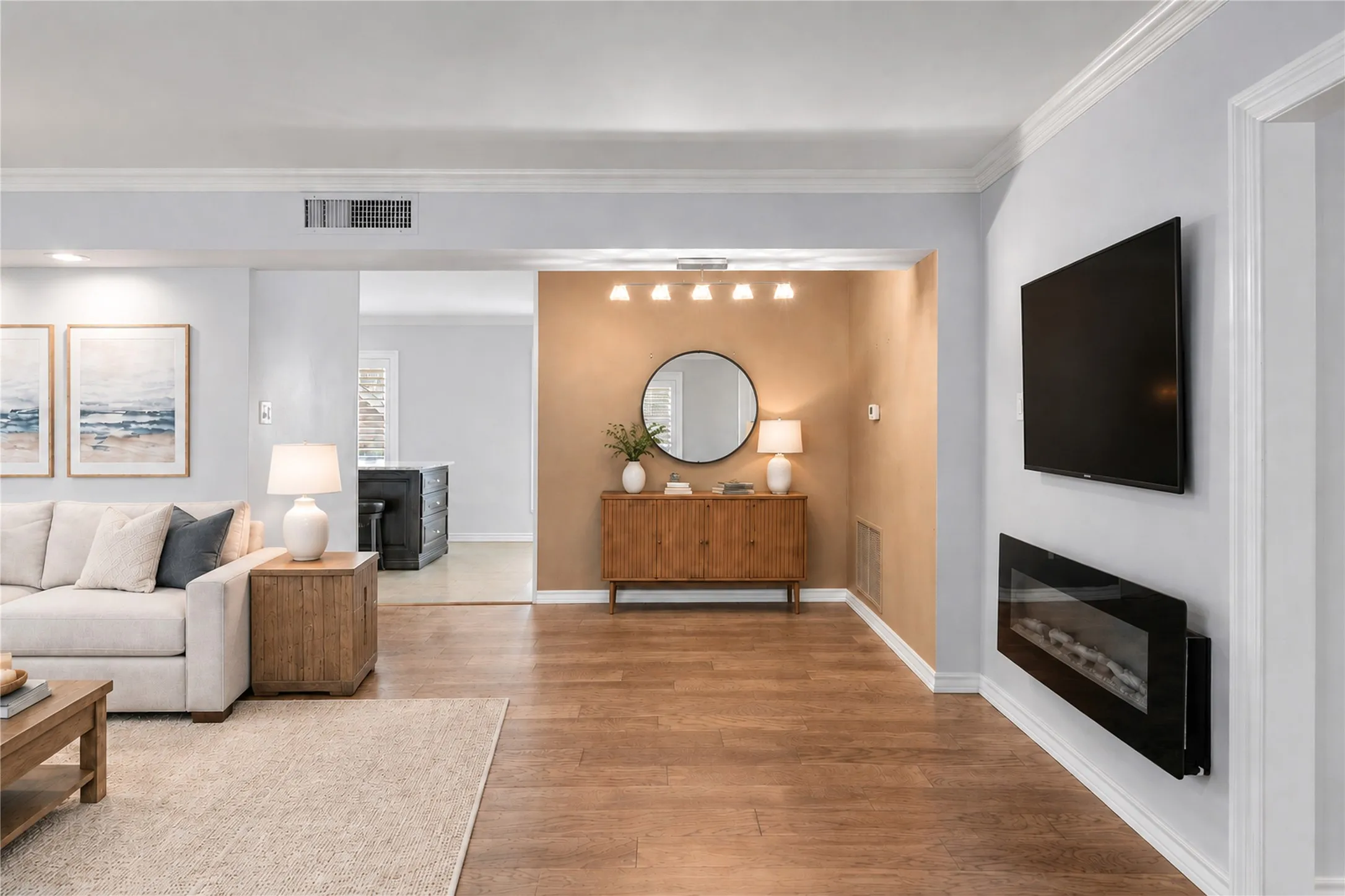 Living area featuring wood-finish flooring, a wall-mounted electric fireplace, crown molding, and a multi-light flush-mount fixture