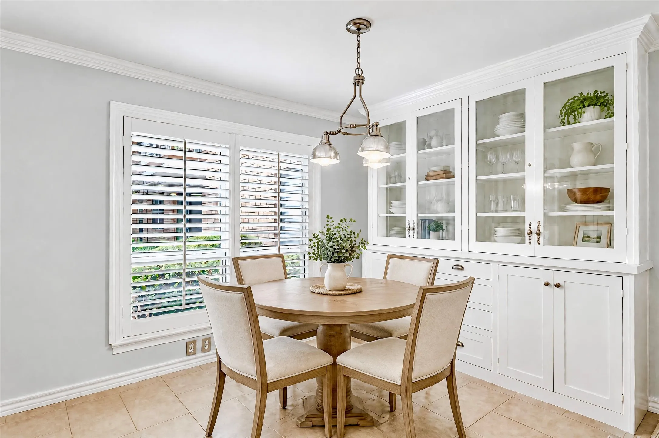 Built-in cabinetry with glass-front display doors, crown molding, tile flooring, and plantation shutters