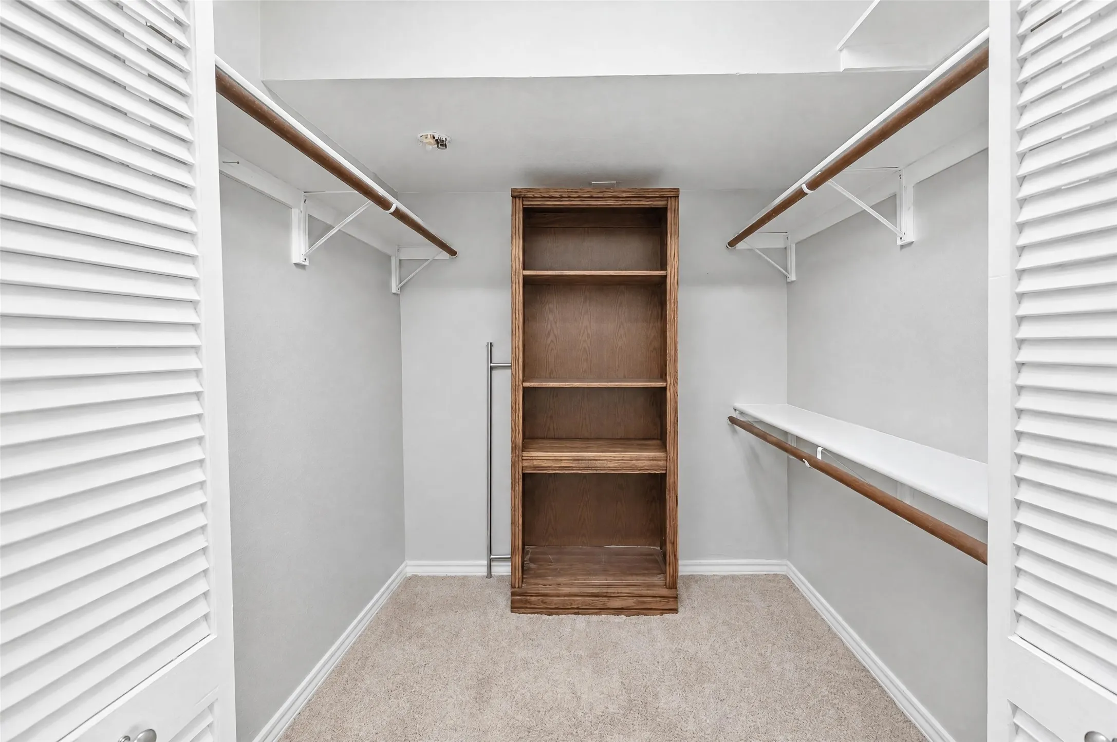 Walk-in storage space featuring built-in wood shelving, dual-level garment rods, and louvered double-door entry