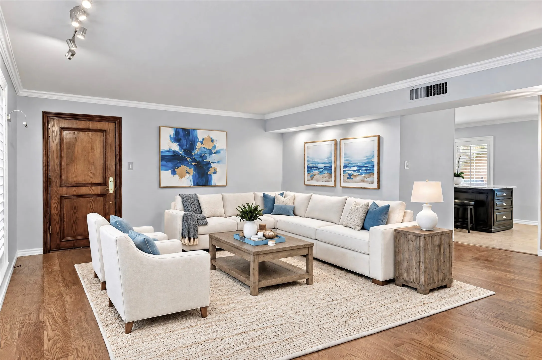 Living area featuring wood-finish flooring, crown molding, a recessed wall niche with integrated lighting, and a multi-panel solid wood entry door