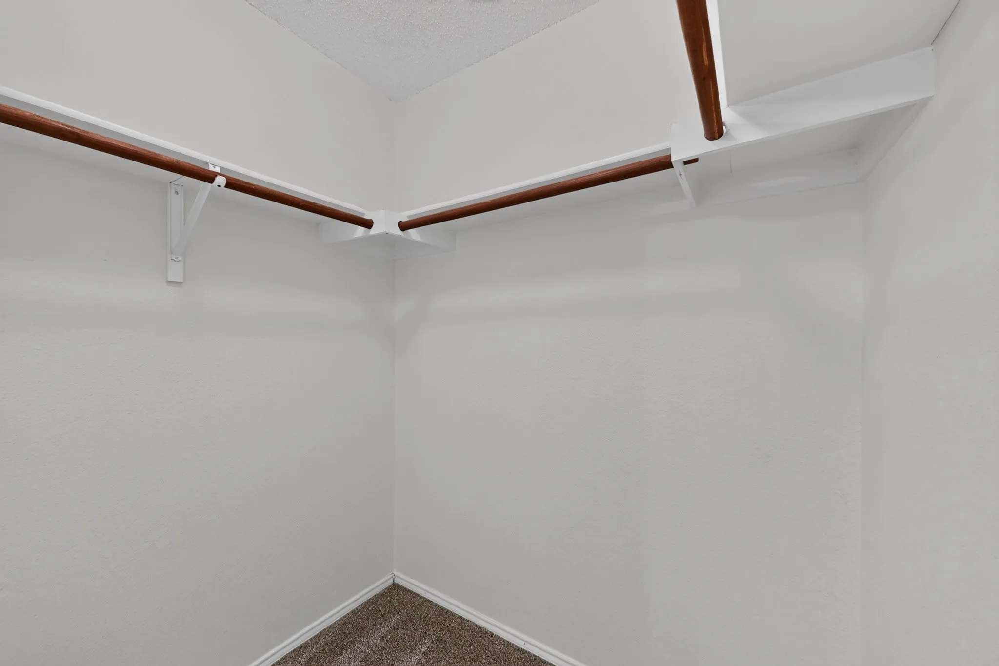 Walk-in closet featuring white wall-mounted shelving with dual wooden hanging rods and wall-to-wall carpeting