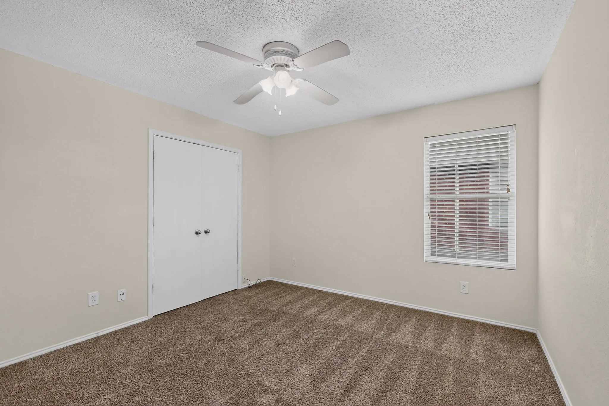 Neutral-toned interior featuring wall-to-wall carpeting, dual-door closet, ceiling fan with integrated light fixture, and window with horizontal blinds