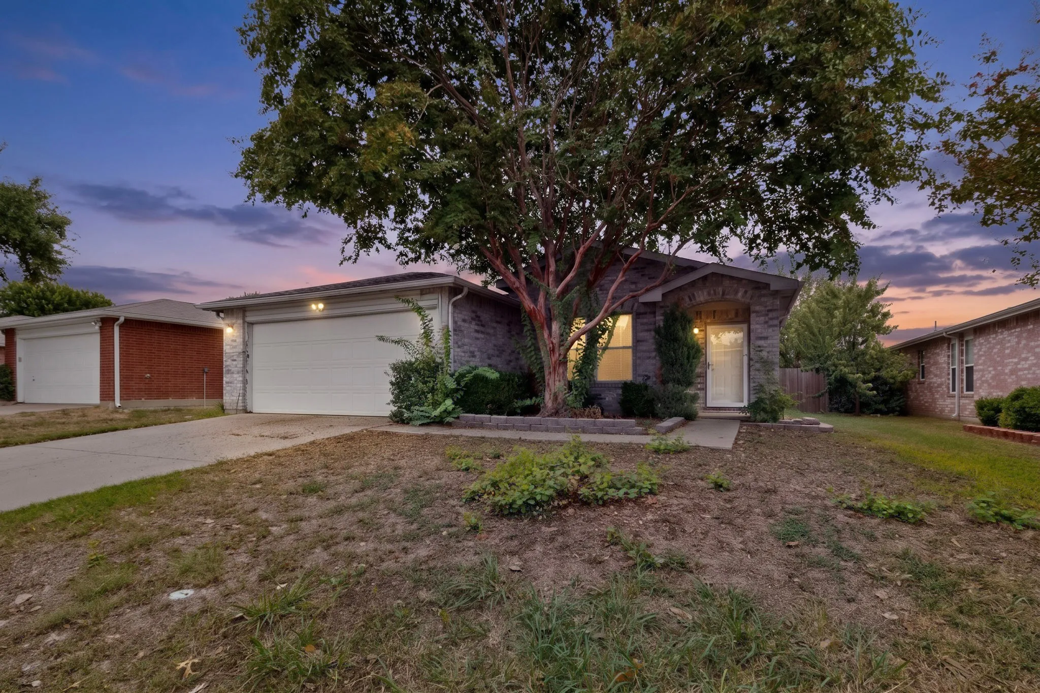 Single-story residence featuring a brick exterior, attached two-car garage, concrete driveway, and mature landscaping