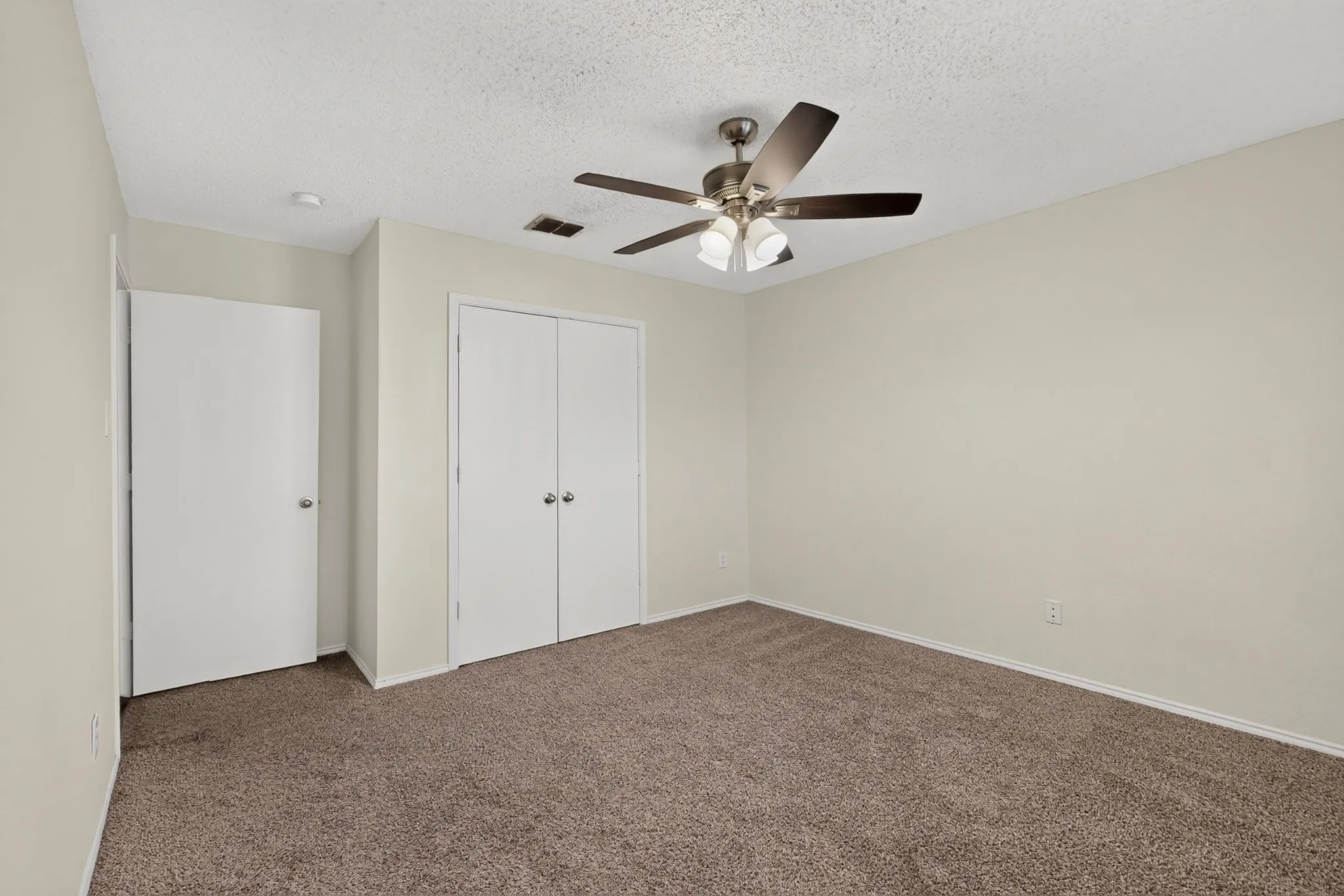 Neutral-toned interior featuring wall-to-wall carpeting, dual-door reach-in closet, and a multi-blade ceiling fan with integrated lighting