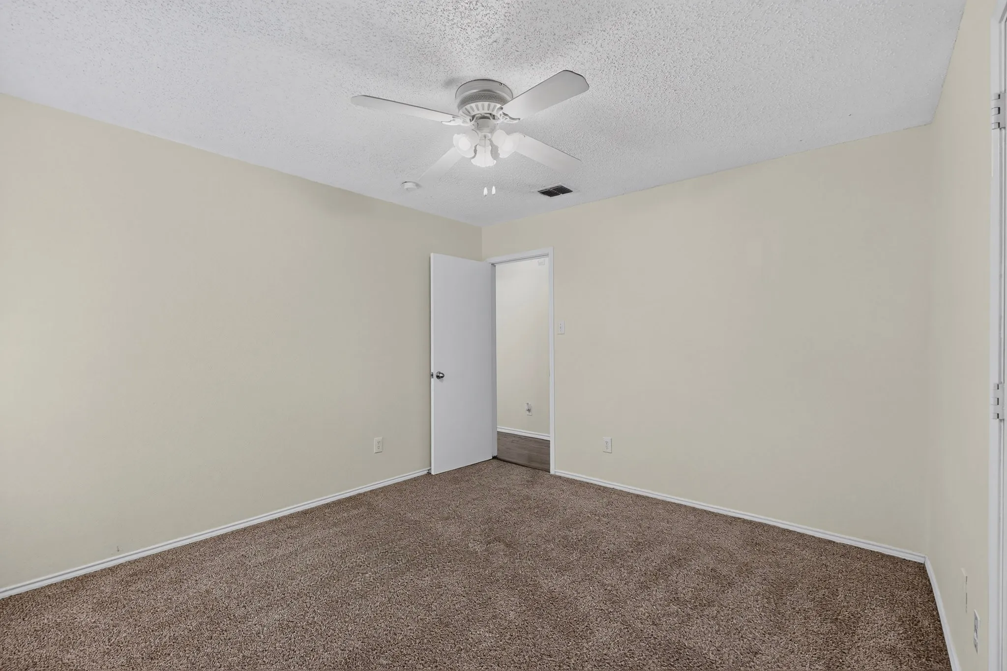 Neutral wall finishes, textured ceiling, wall-to-wall carpeting, and a multi-blade ceiling fan with integrated lighting