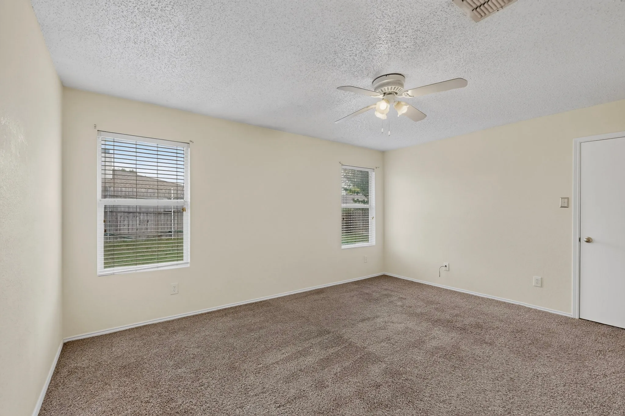 Neutral-toned walls, textured ceiling, carpeting, ceiling-mounted fan with light fixture, and windows with horizontal blinds