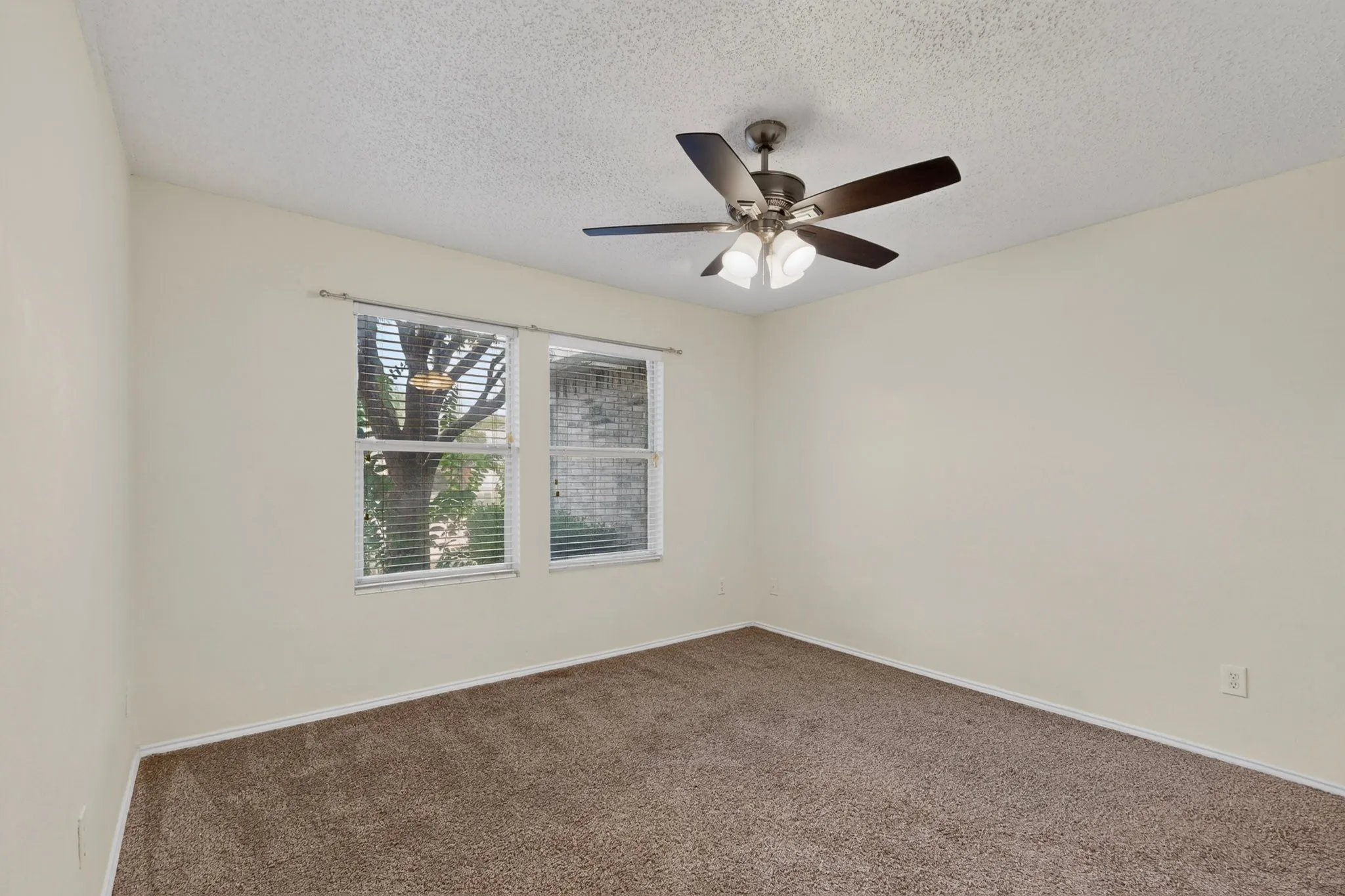 Neutral-toned walls, carpeting, dual windows with horizontal blinds, and a multi-blade ceiling fan with integrated lighting
