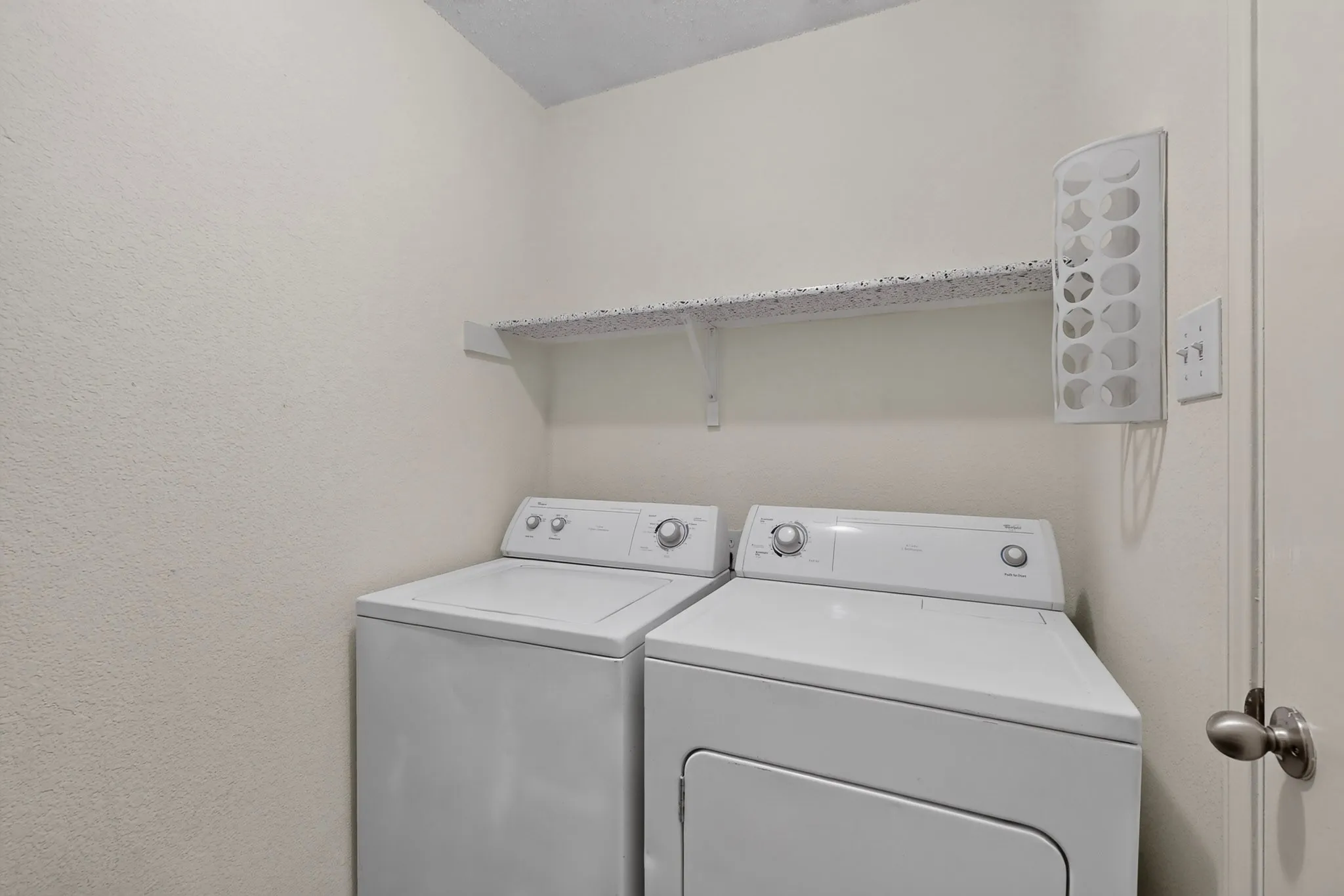 Dedicated laundry alcove featuring white top-load washer and dryer, mounted storage shelving, and wall-affixed lighting fixture