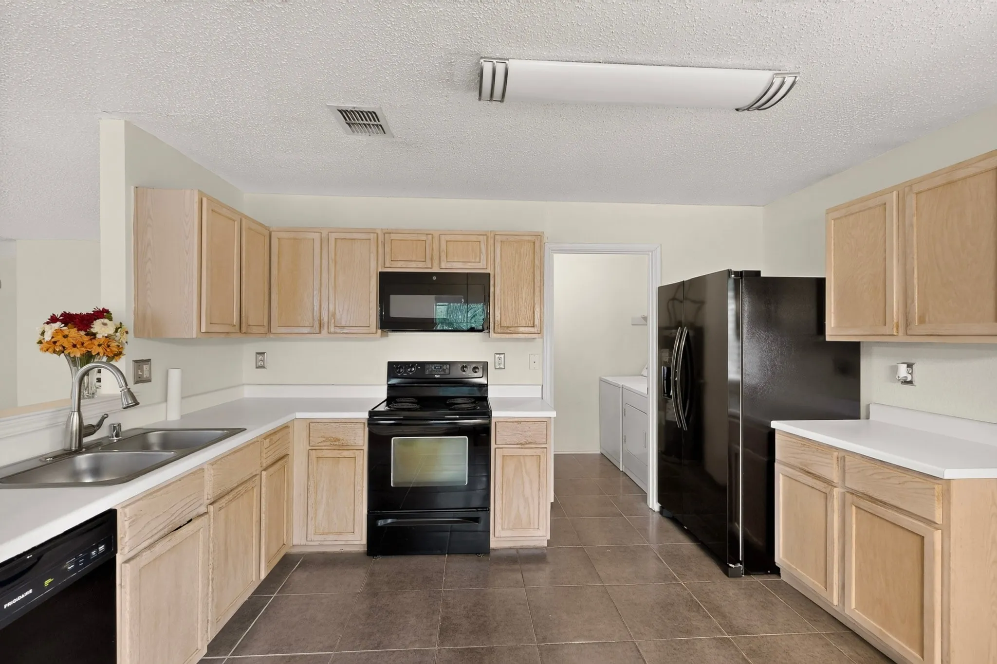 Kitchen featuring light-finish cabinetry, white countertops, large-format tile flooring, a black suite of appliances, and a stainless steel dual-basin sink