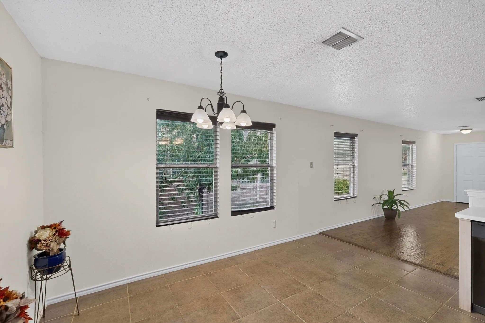Open concept interior featuring ceramic tile flooring, wood-finish flooring, multi-pane windows with horizontal blinds, and a five-light chandelier