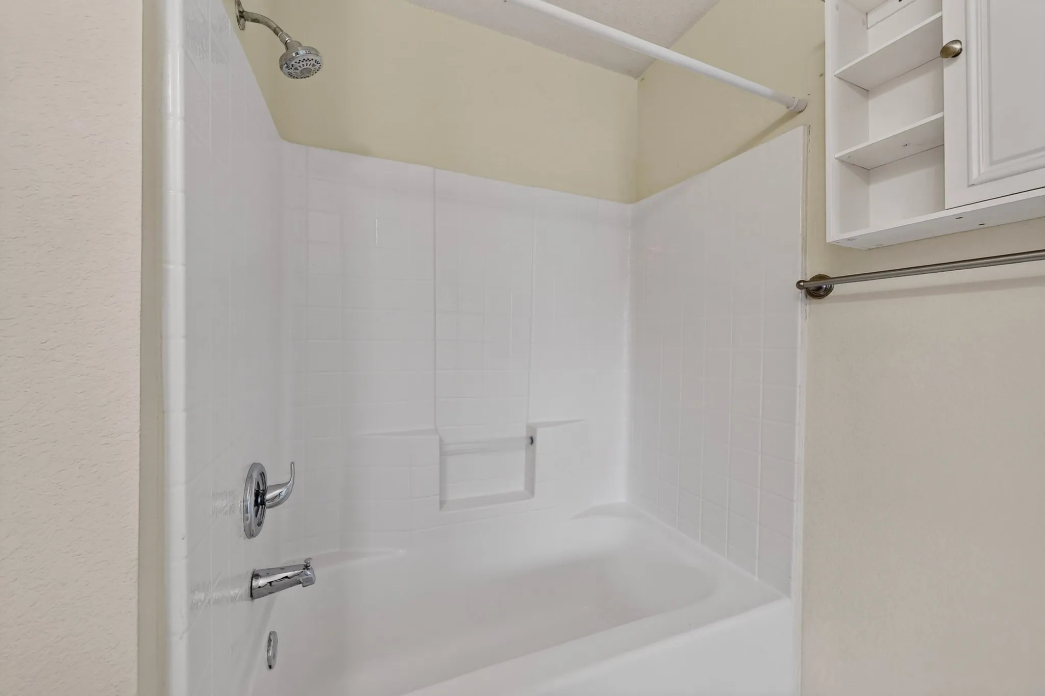 Bathtub featuring a white tiled surround with integrated shelving, chrome-finish fixtures, and built-in wall-mounted cabinetry