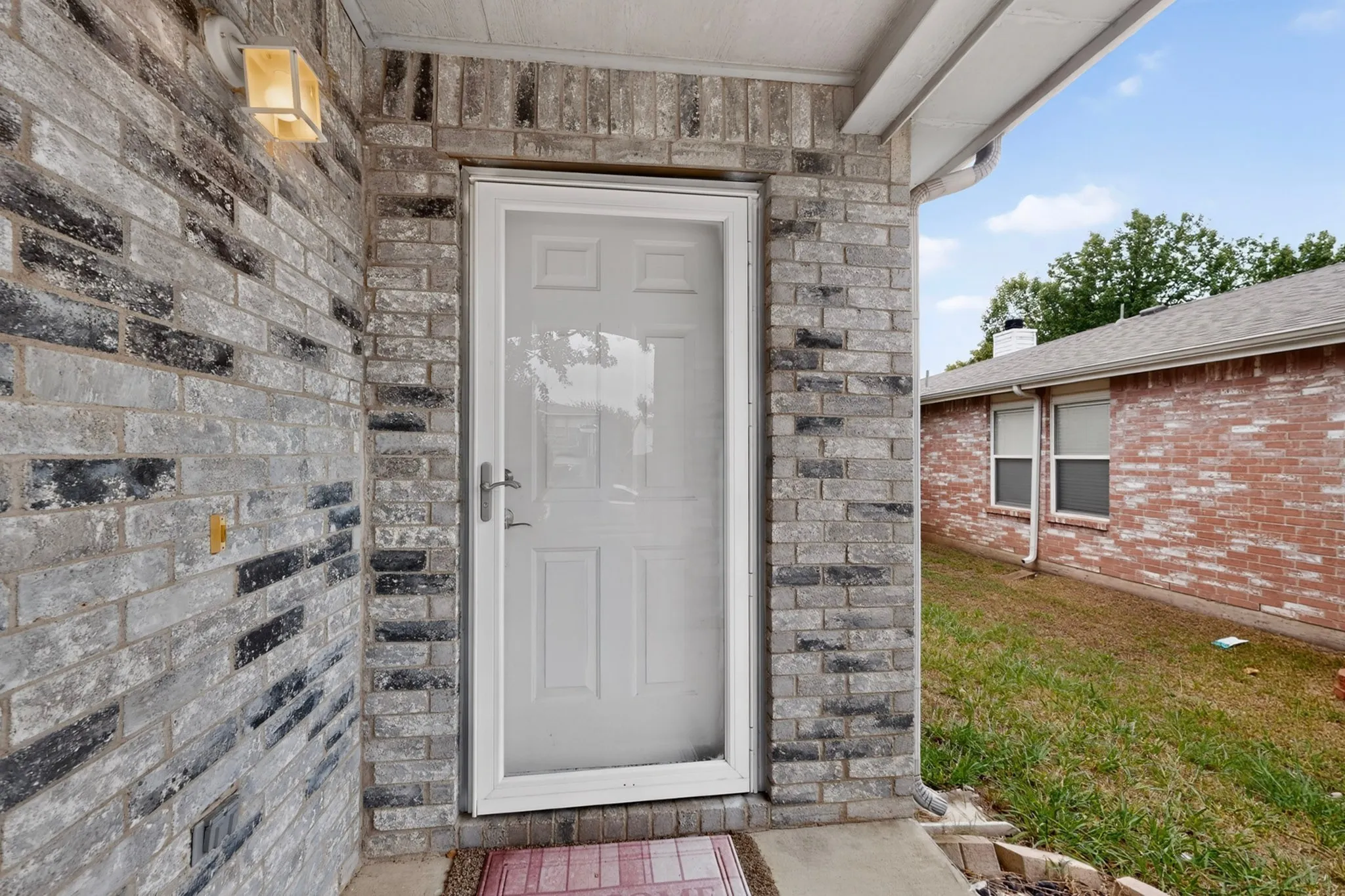 Entryway featuring multi-toned grey brick facade, white storm door, and mounted exterior lighting fixture
