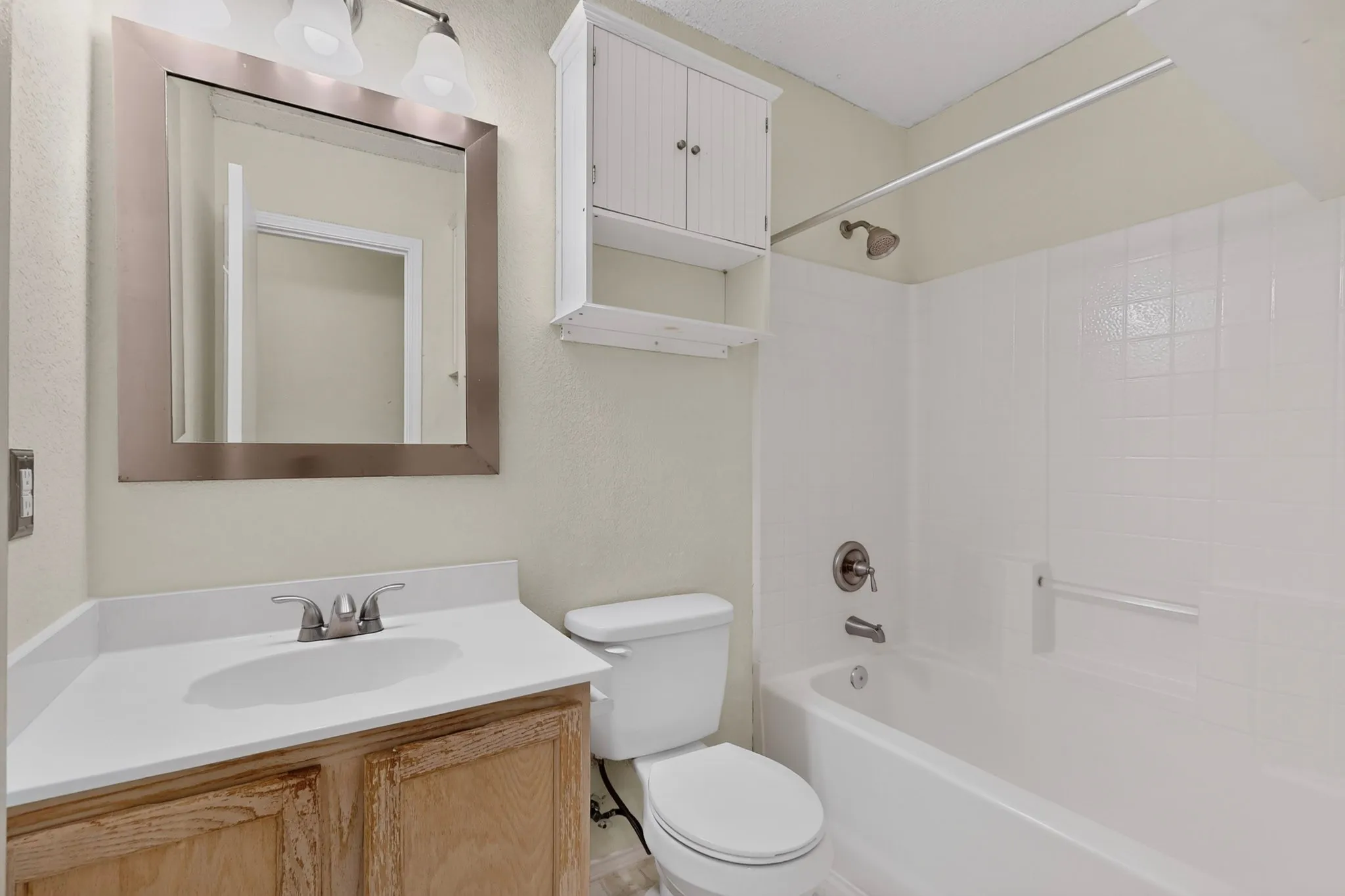 Bathroom featuring a vanity with a white solid-surface countertop, an integrated sink, a wall-mounted wooden cabinet, and a tiled tub-and-shower combination
