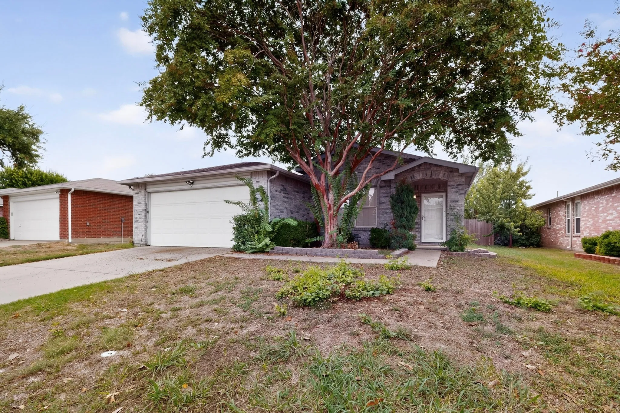 Single-story brick exterior featuring a front-facing attached two-car garage, concrete driveway, and mature landscaping
