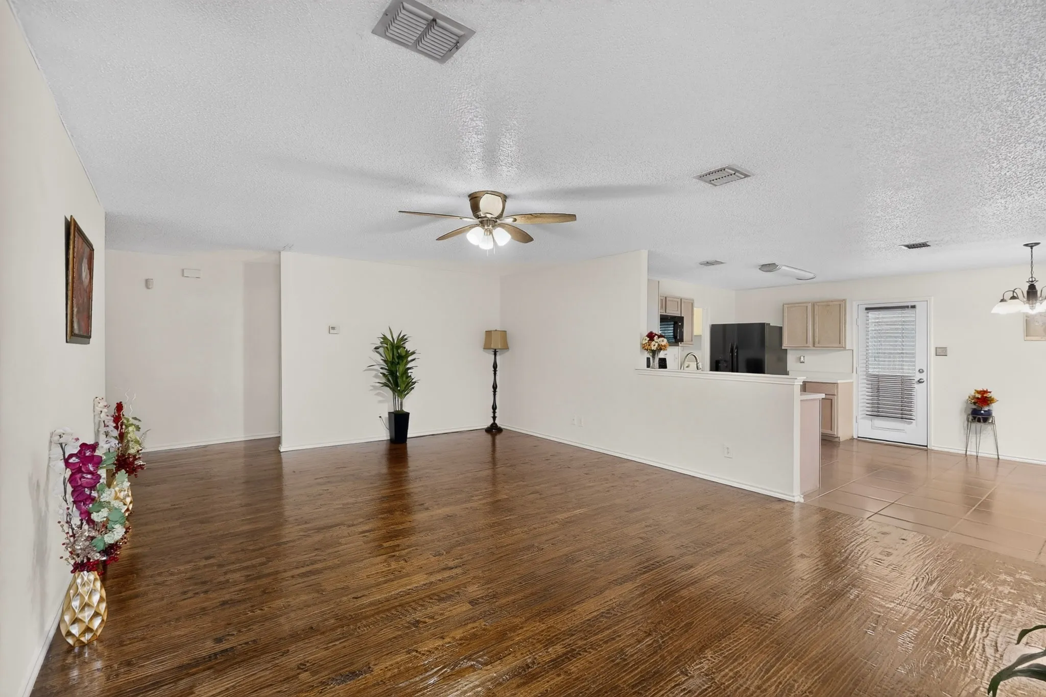 Open floor plan featuring wood-finish flooring, neutral wall paint, recessed ceiling lighting, a ceiling fan with integrated light fixture, and ceramic tile flooring in the kitchen area