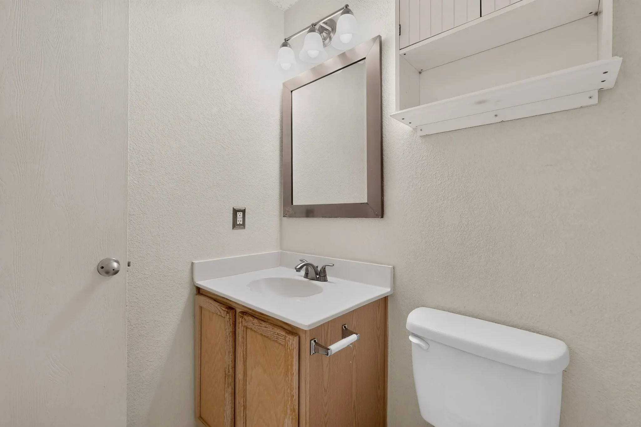 Vanity cabinet with integrated solid-surface countertop and undermount sink, brushed-nickel hardware, framed wall mirror, three-light vanity fixture, and white wall-mounted cabinetry
