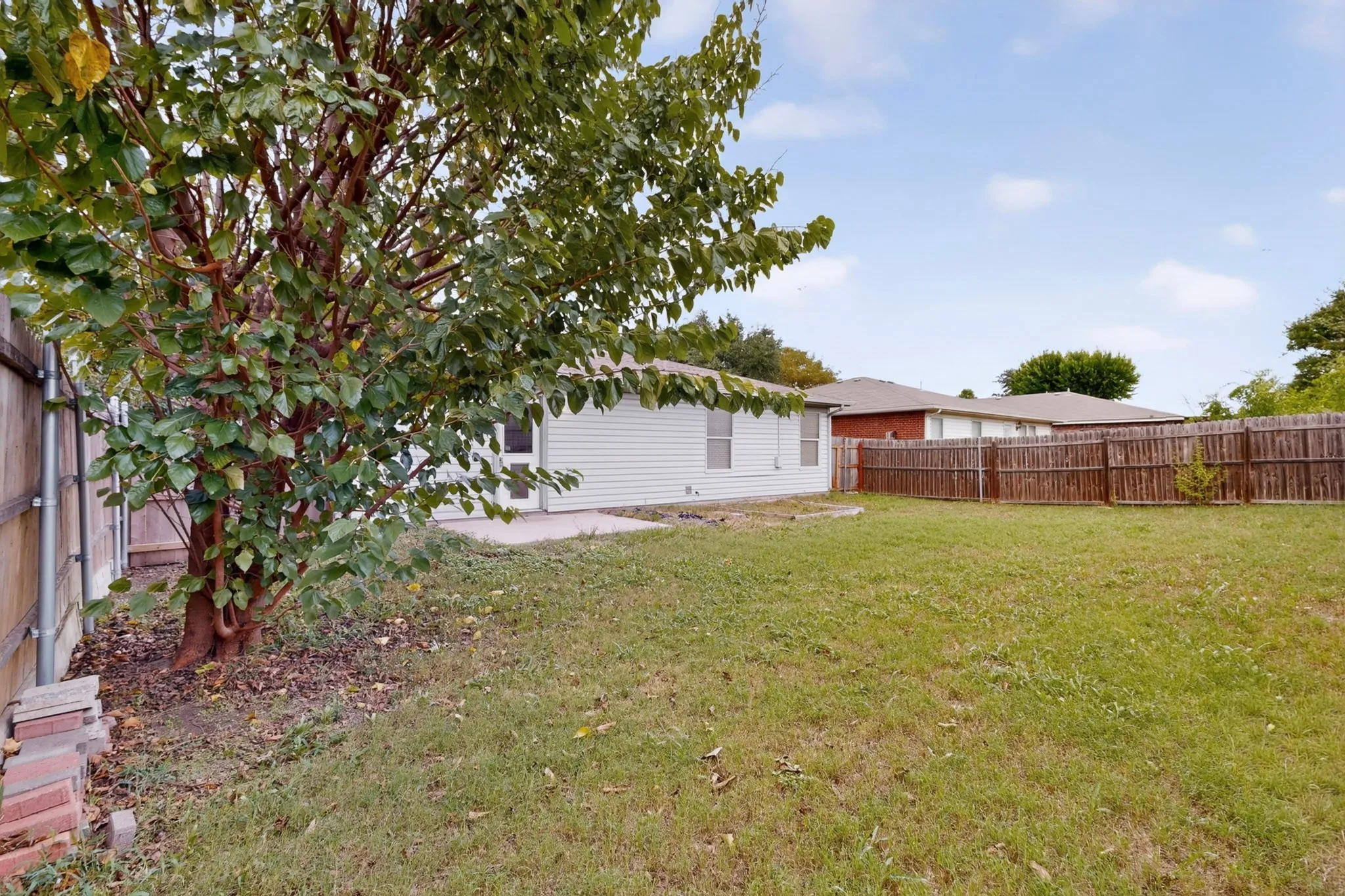 Backyard featuring a concrete patio, wood privacy fencing, and mature trees
