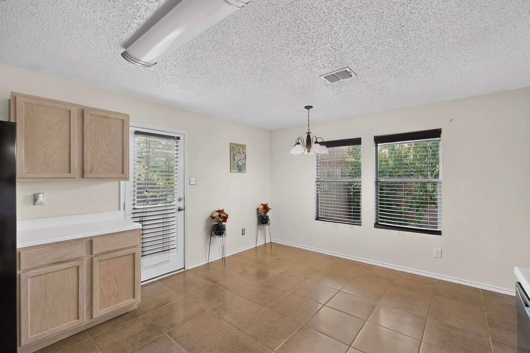 Neutral-toned tile flooring, light wood-finish cabinetry, solid surface countertops, a multipane glass-panel exterior door, and hanging pendant lighting
