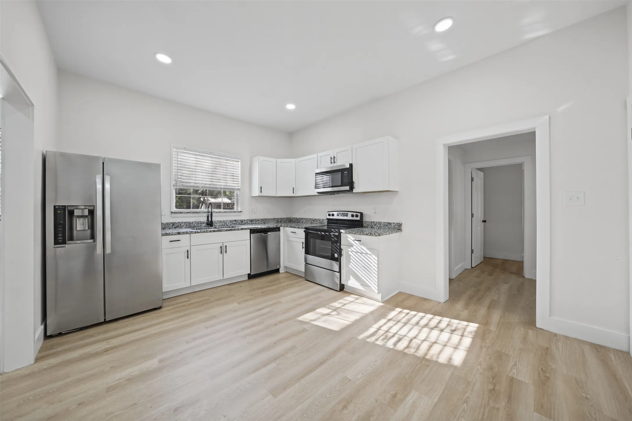 Kitchen featuring white shaker-style cabinetry, stone-finish countertops, stainless steel appliances, and wood-finish flooring