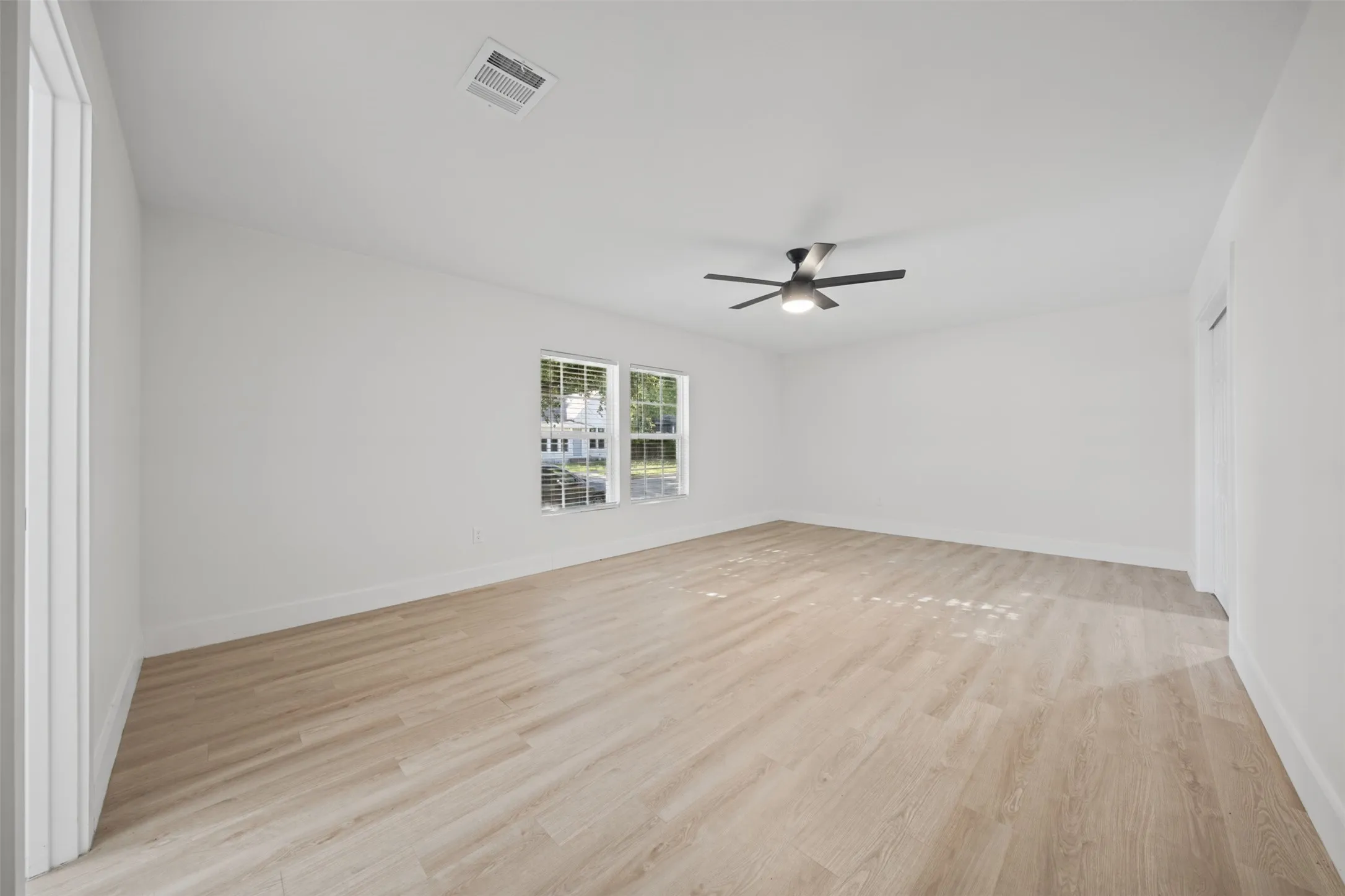 Spacious room featuring wood-finish flooring, neutral walls, dual-pane windows, and a ceiling-mounted light fixture with a fan