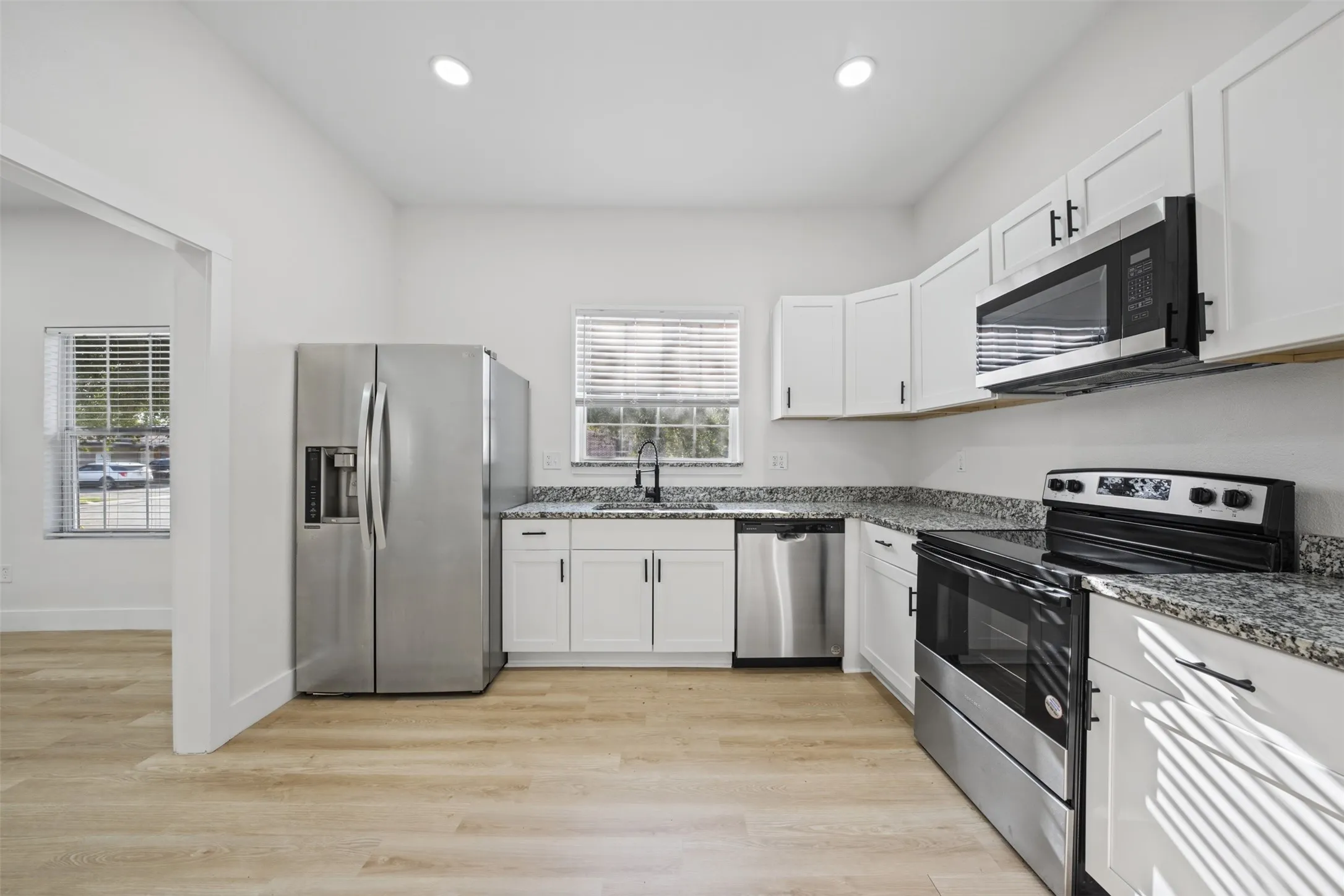 Kitchen featuring white cabinetry, speckled stone countertops, stainless steel appliances, and wood-finish flooring