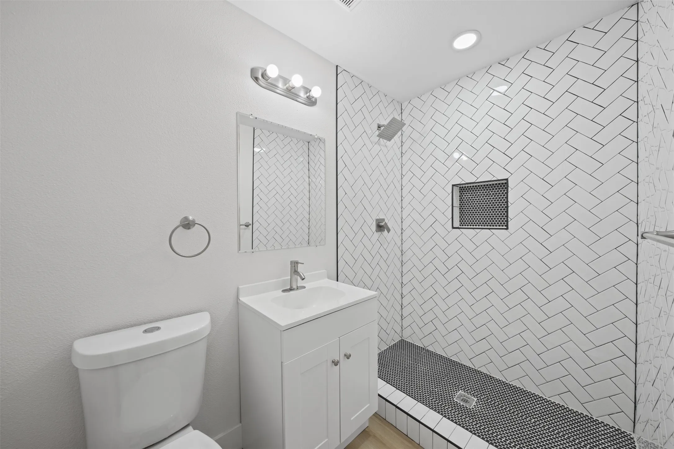 Bathroom featuring a white vanity cabinet, herringbone-patterned wall tile, recessed shower niche, and dark geometric floor tile