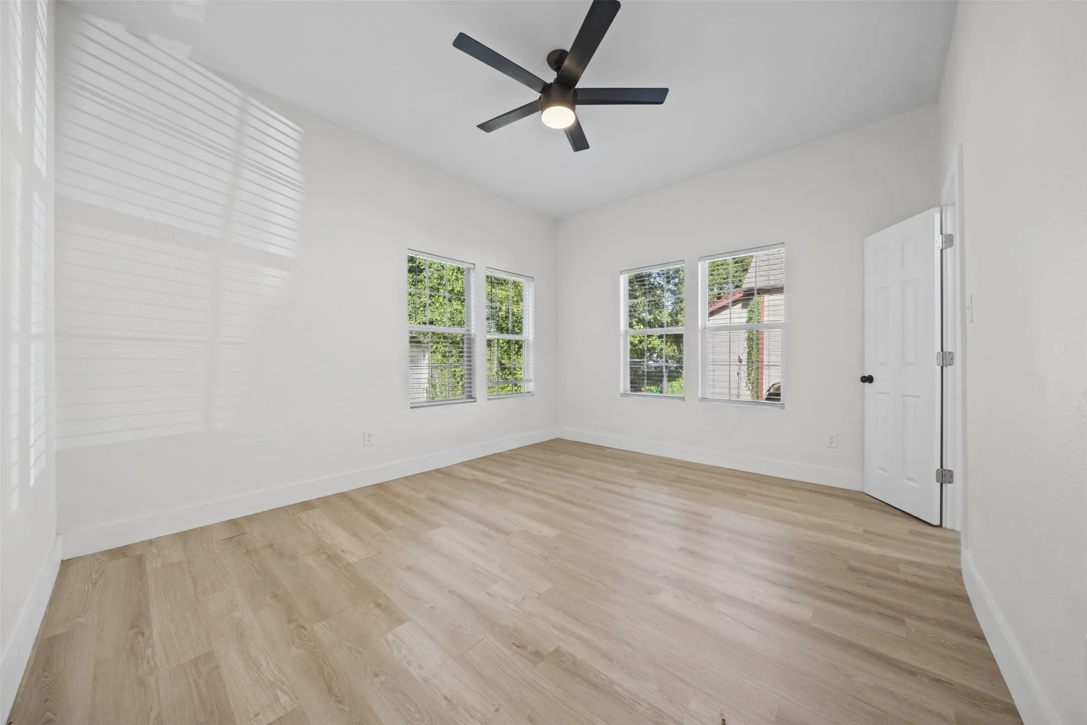 Room featuring wood-finish flooring, a matte black ceiling fan with integrated lighting, and multiple windows