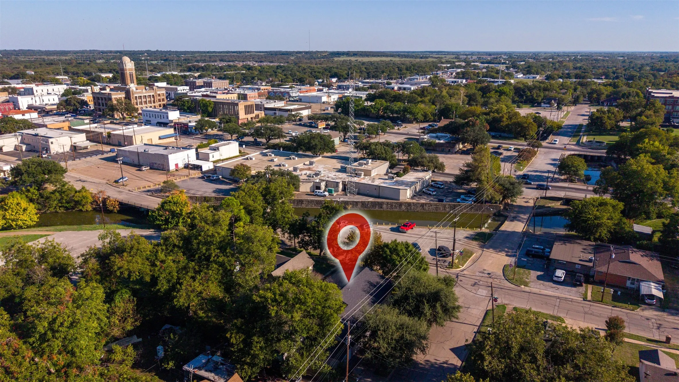 Aerial perspective of the property featuring a localized location marker, mature tree canopy, and proximity to municipal infrastructure and thoroughfares