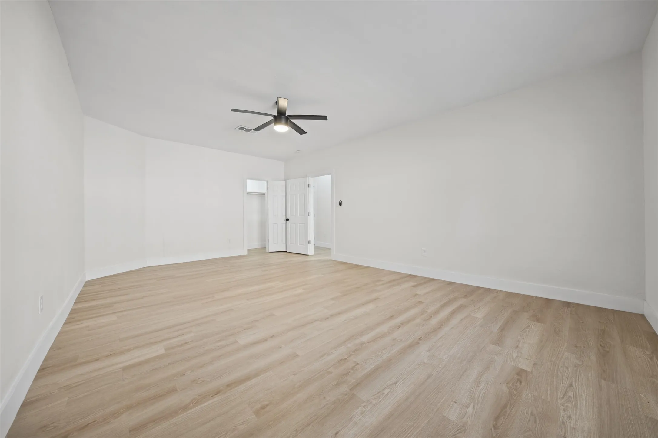 Spacious room featuring light-toned wood-finish flooring, neutral walls, and a ceiling-mounted fan with integrated lighting