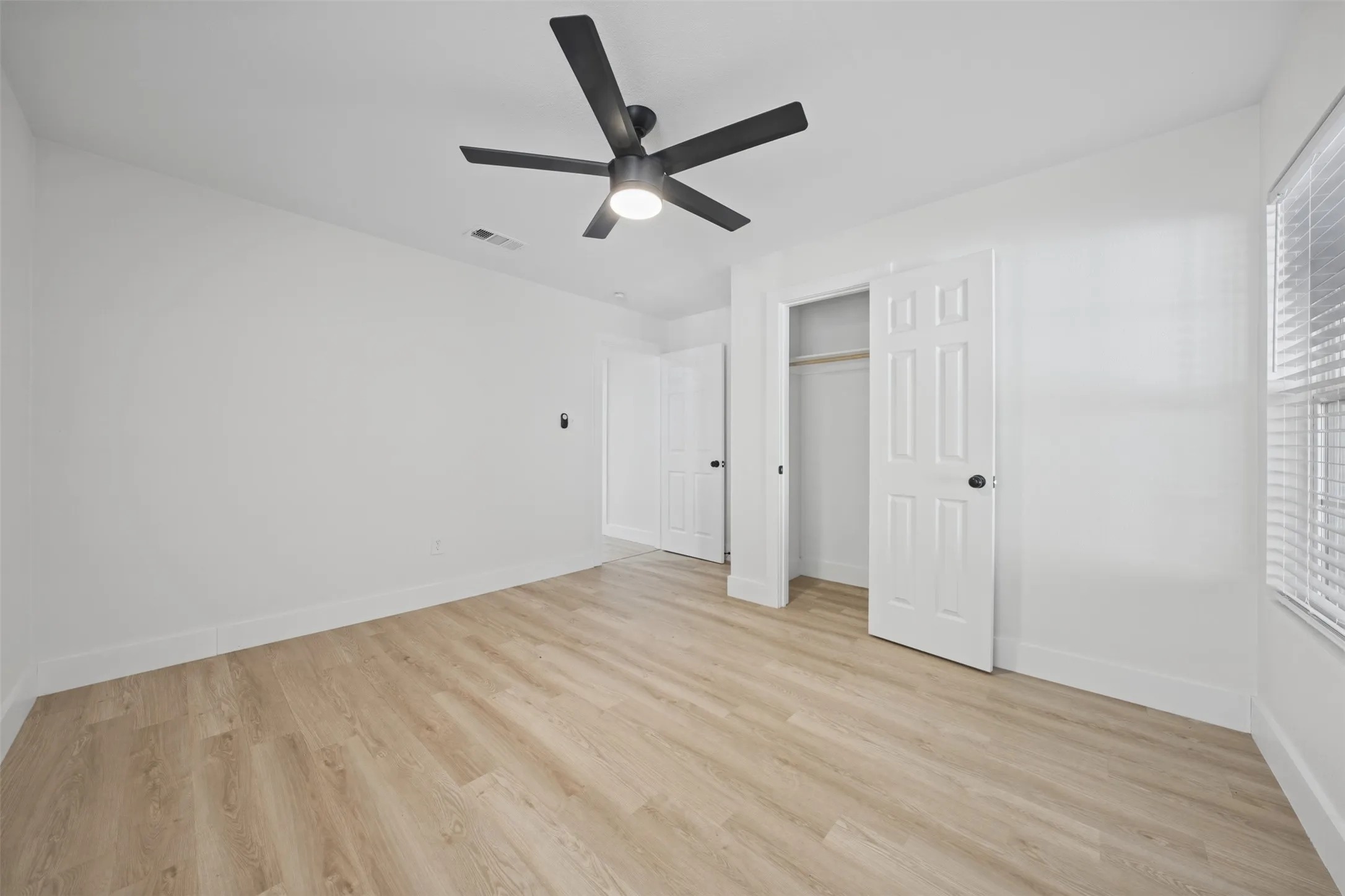 Room featuring wood-finish flooring, a matte black multi-blade ceiling fan with integrated lighting, and a closet with six-panel doors