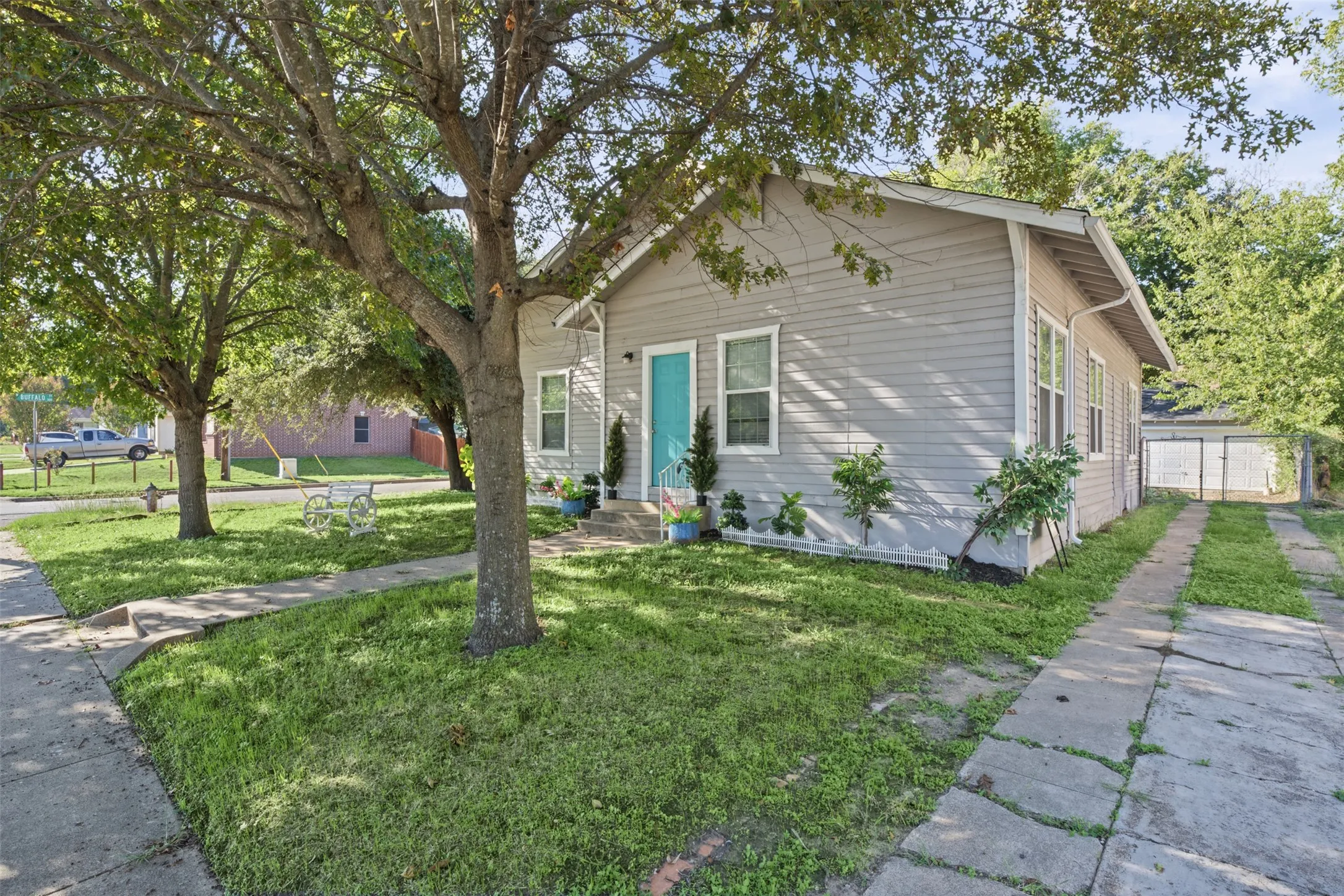 Single-story residence featuring light-toned horizontal siding, a central entry door with a vibrant finish, white-framed windows, and an expansive front lawn with mature shade trees