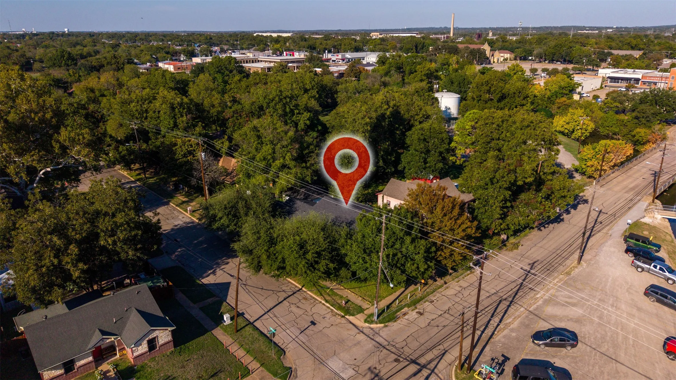 Aerial perspective of a corner lot property featuring mature shade trees, established landscaping, and proximity to municipal infrastructure and thoroughfares