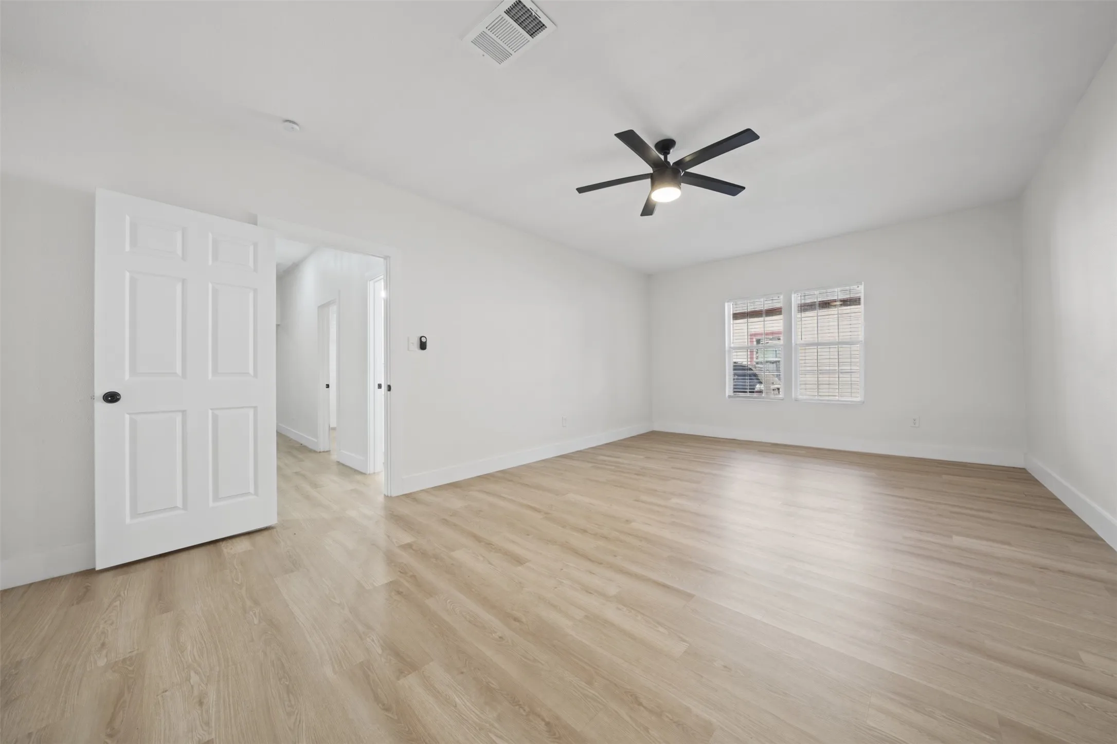 Neutral-toned wood-finish flooring, matte black ceiling fan with integrated lighting, dual windows, and white paneled interior door