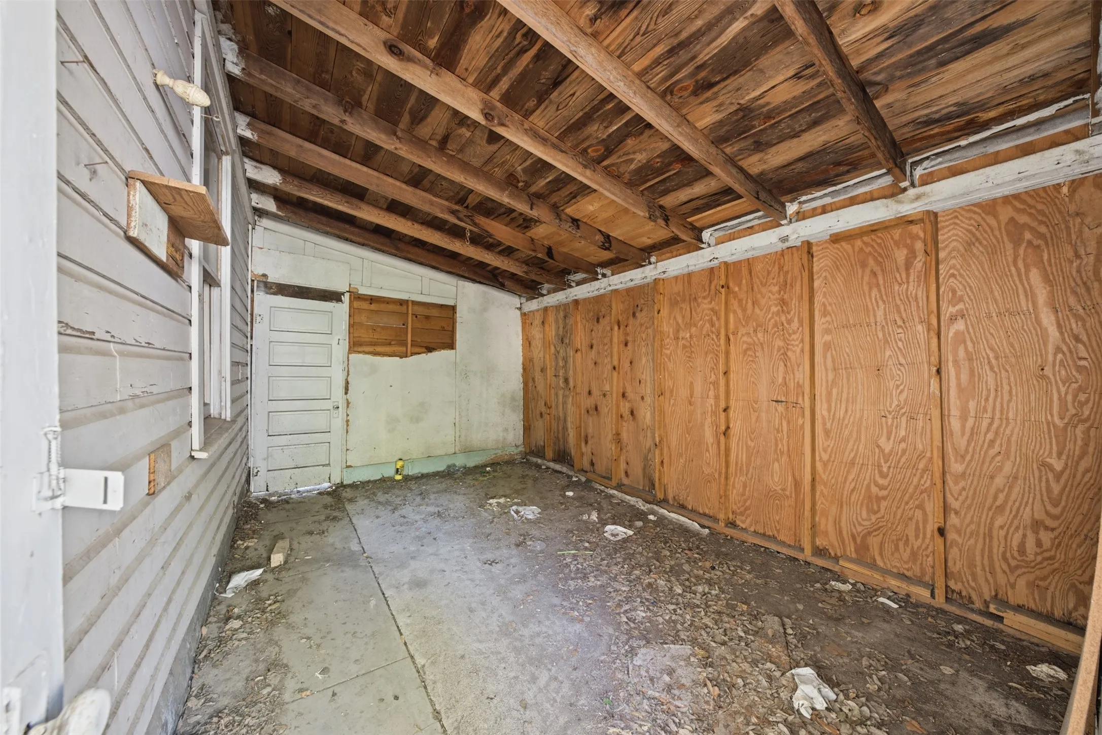 Enclosed porch featuring exposed wood beam ceiling, wood-paneled walls, a single-entry door, and concrete flooring