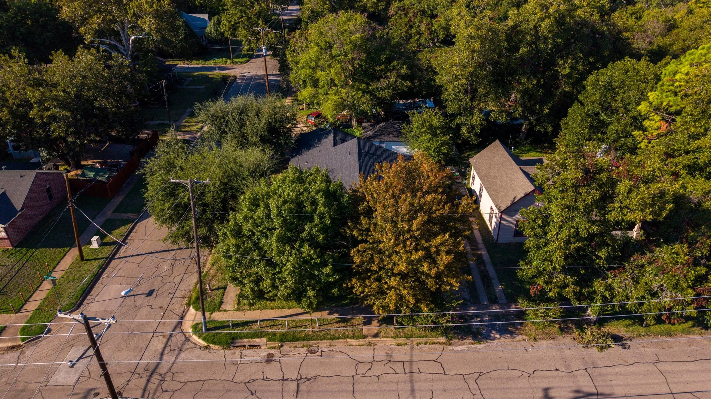 Aerial perspective of a property featuring mature trees, a private concrete driveway, and a shingled roof