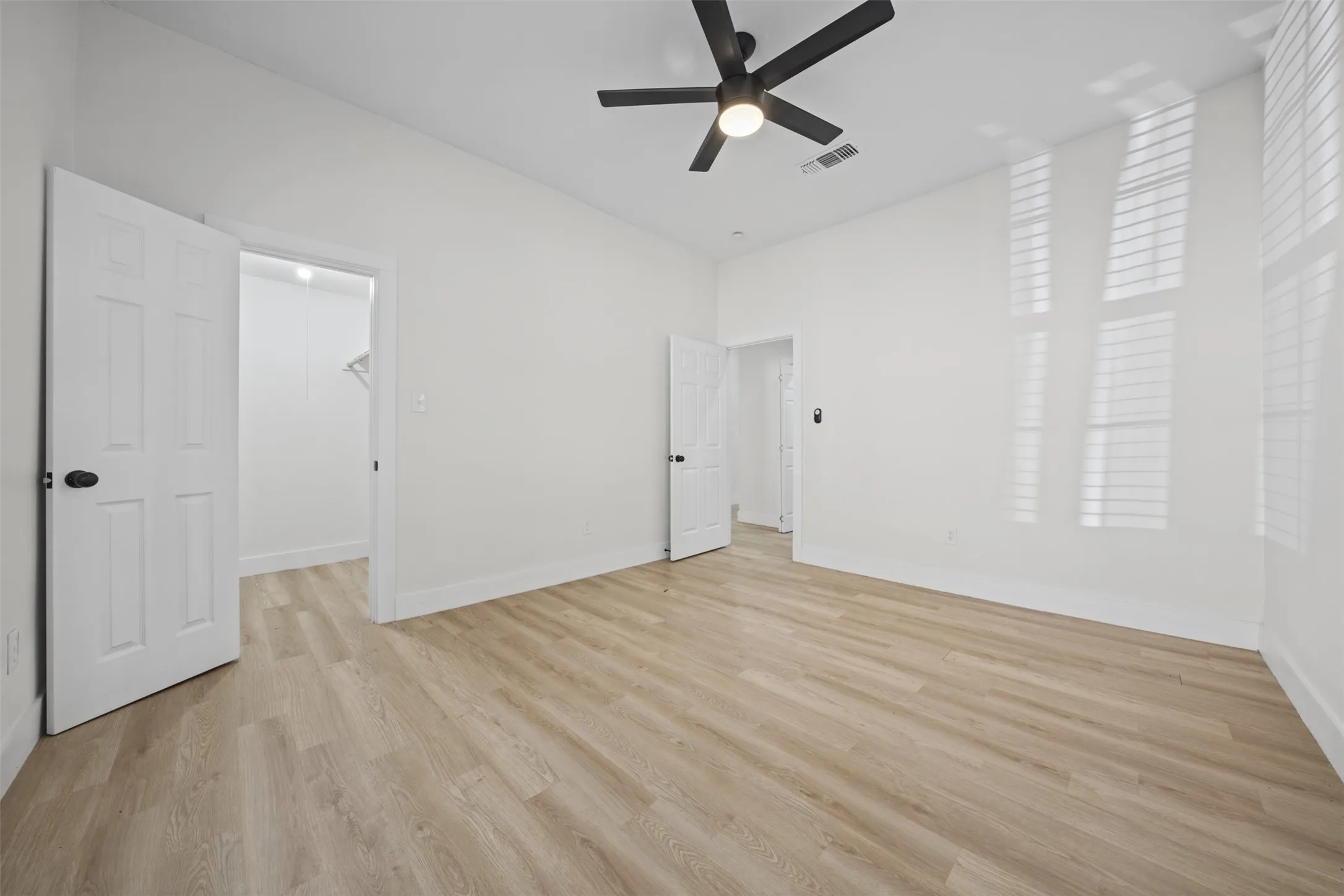 High ceilings with a matte black ceiling fan, wood-finish flooring, and white plantation shutters