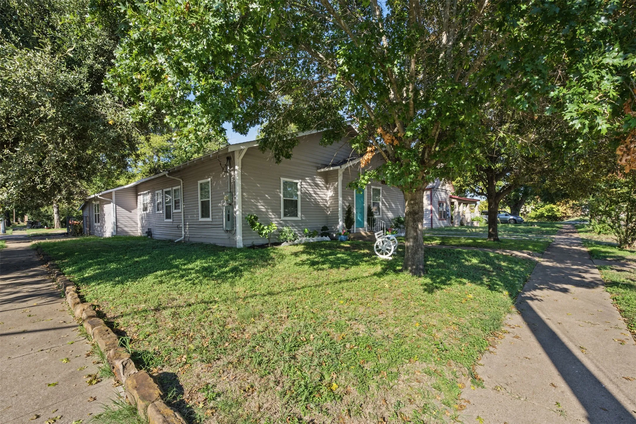 Single-story exterior with horizontal siding, multiple windows, stone edging along the lawn, and mature trees