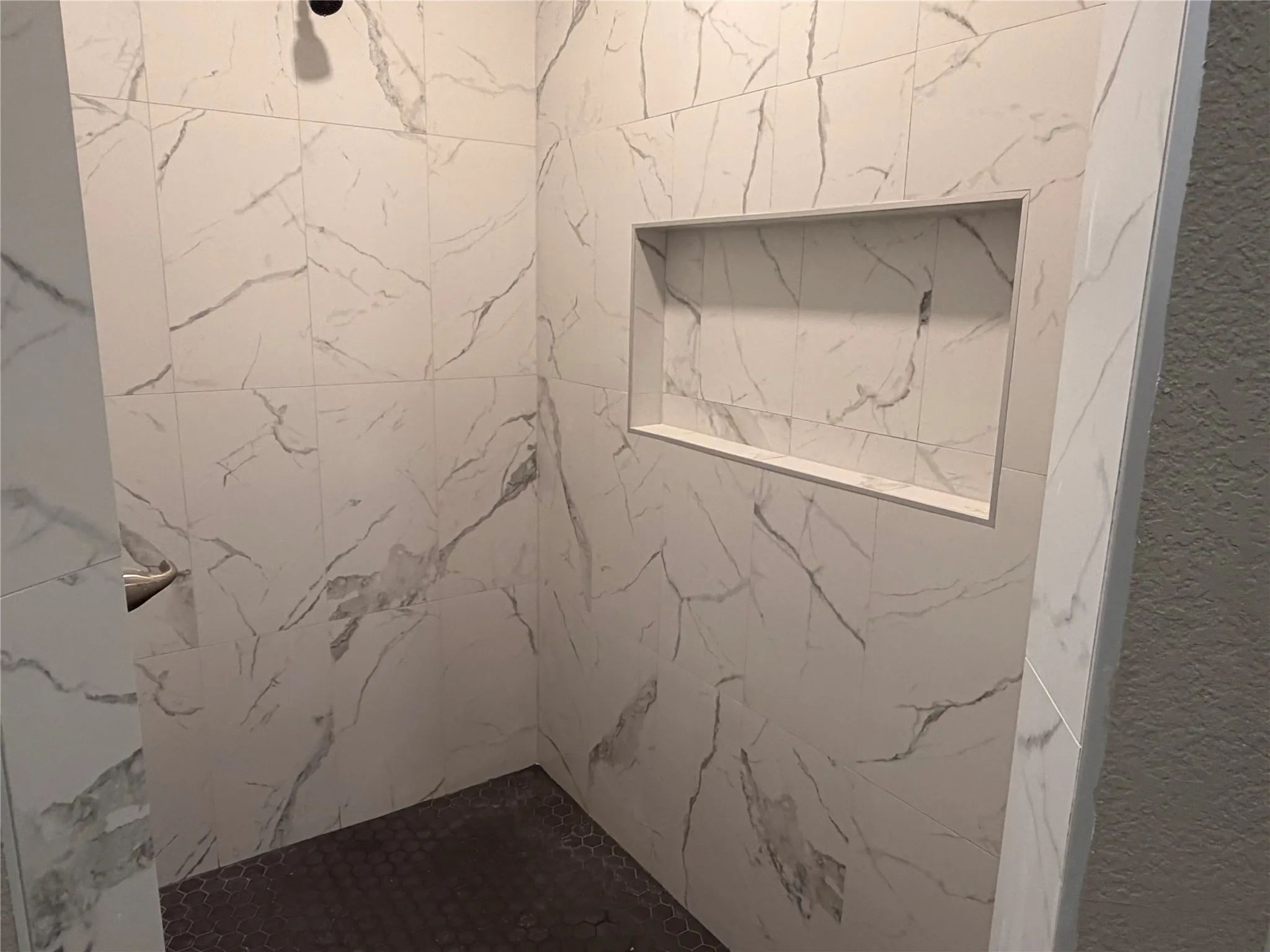 Walk-in shower featuring floor-to-ceiling stone-pattern tile, a built-in recessed wall niche, and hexagonal floor tile
