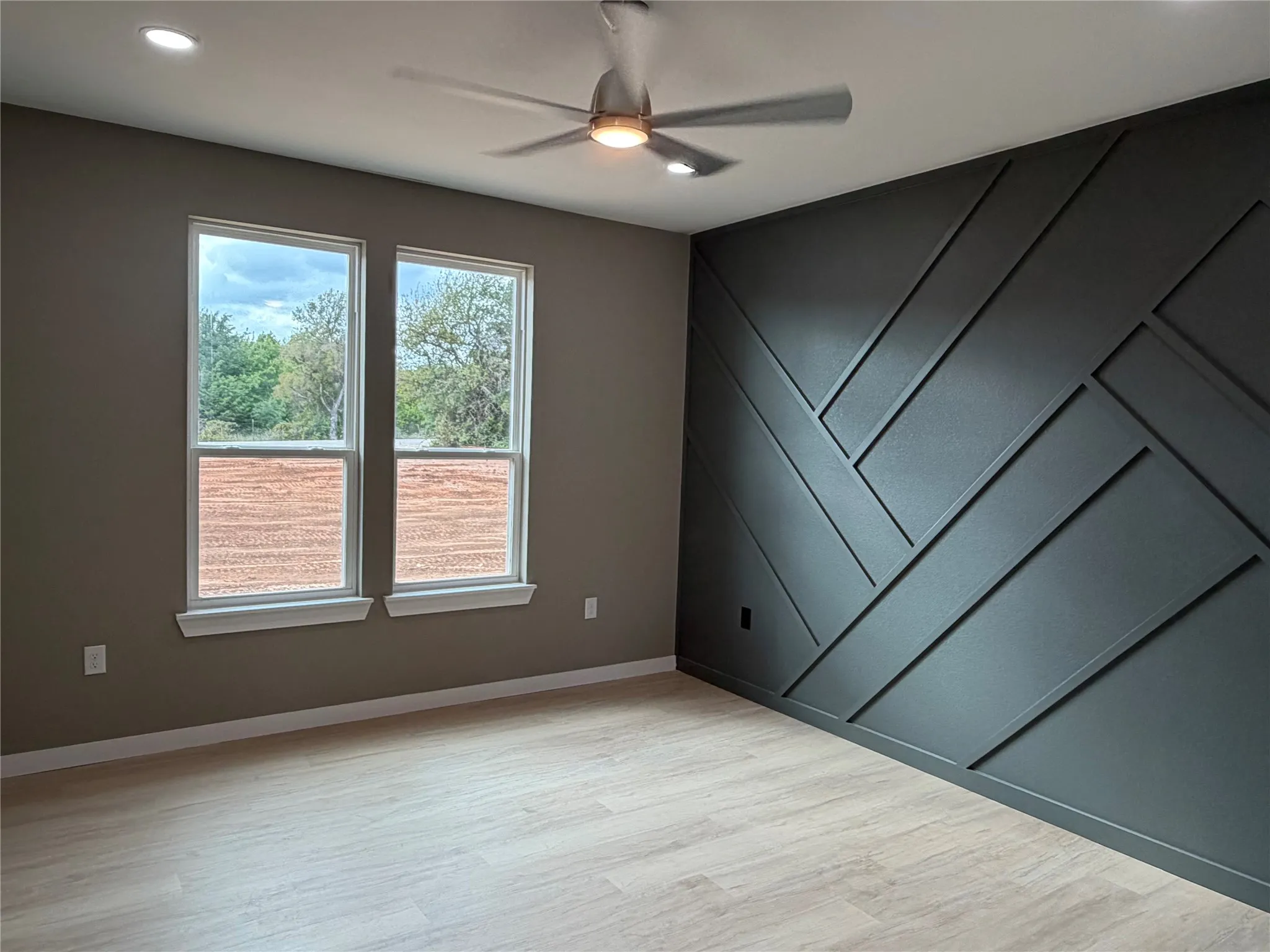Primary Bedroom Geometric accent wall featuring a custom wood trim design, wood-finish flooring, dual-pane windows, and a ceiling fan with integrated lighting
