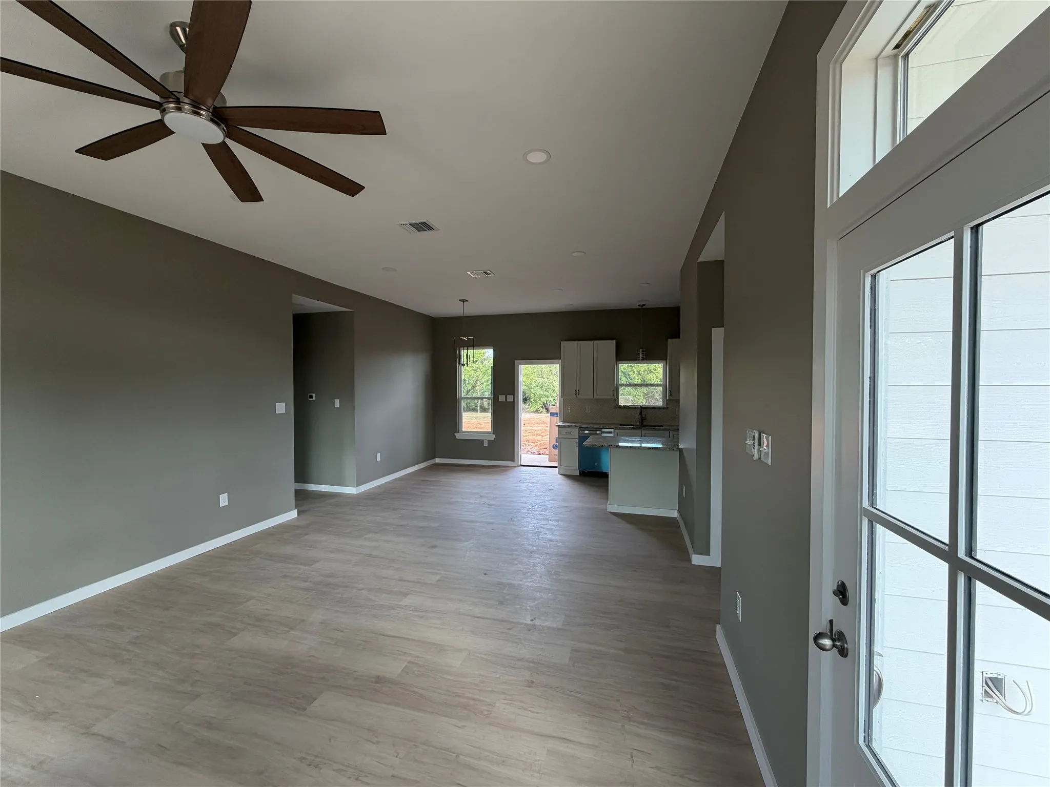 Open interior space featuring wood-finish flooring, recessed lighting, a multi-blade ceiling fan, and a transom window above a glass-paneled exterior door