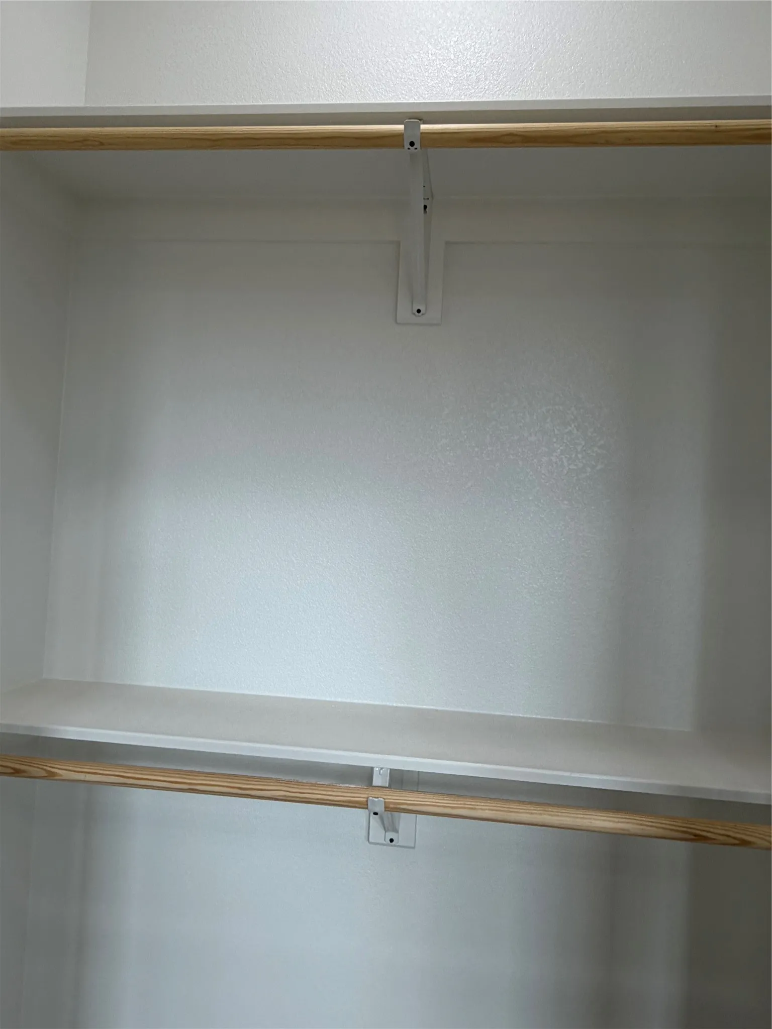 Closet featuring dual wood-finish hanging rods and fixed shelving with white support brackets
