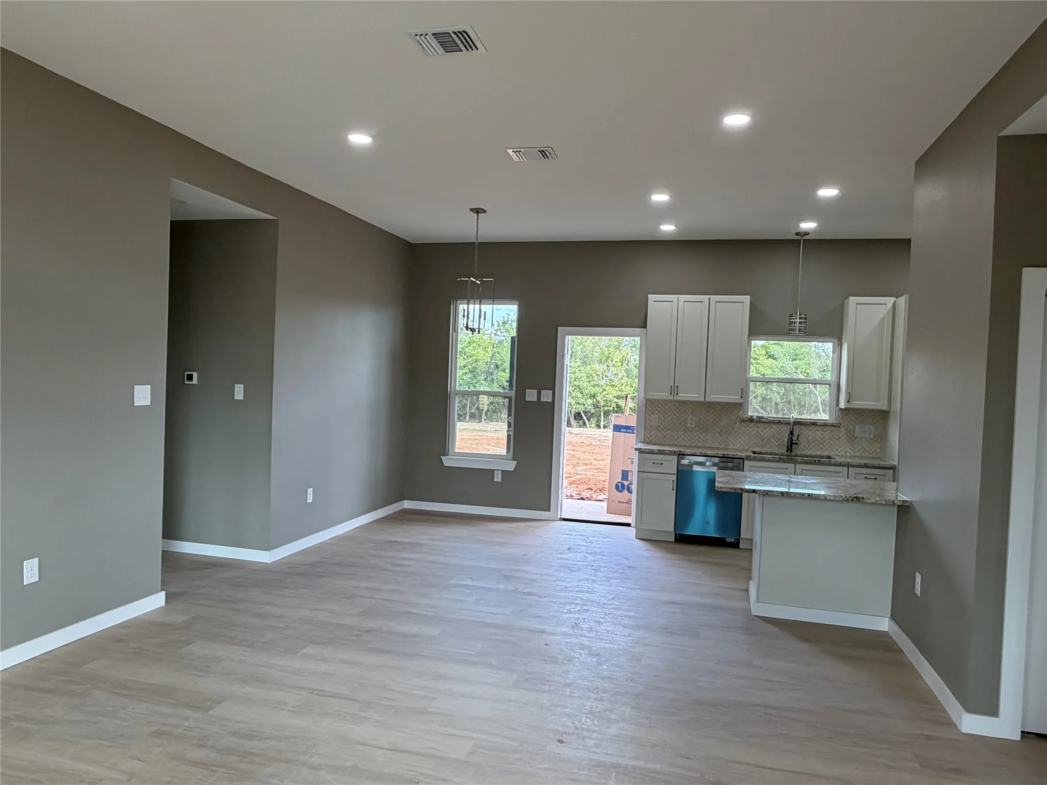Open-concept interior featuring wood-finish flooring, recessed lighting, white cabinetry, a stone-patterned countertop, and a peninsula with under-cabinet storage