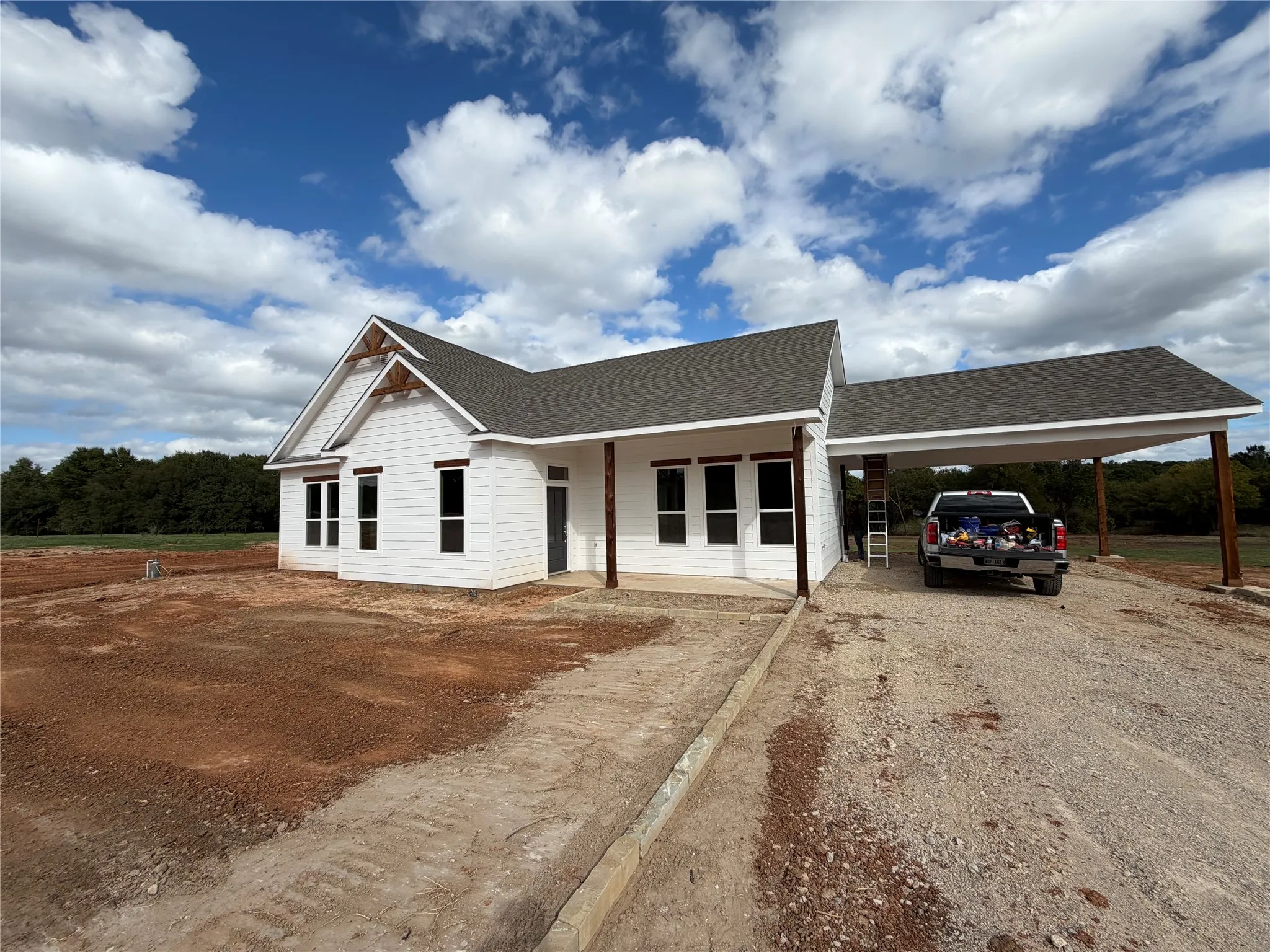 Single-story residence featuring white horizontal siding, a gabled roofline with timber truss accents, a covered front porch, and an attached carport