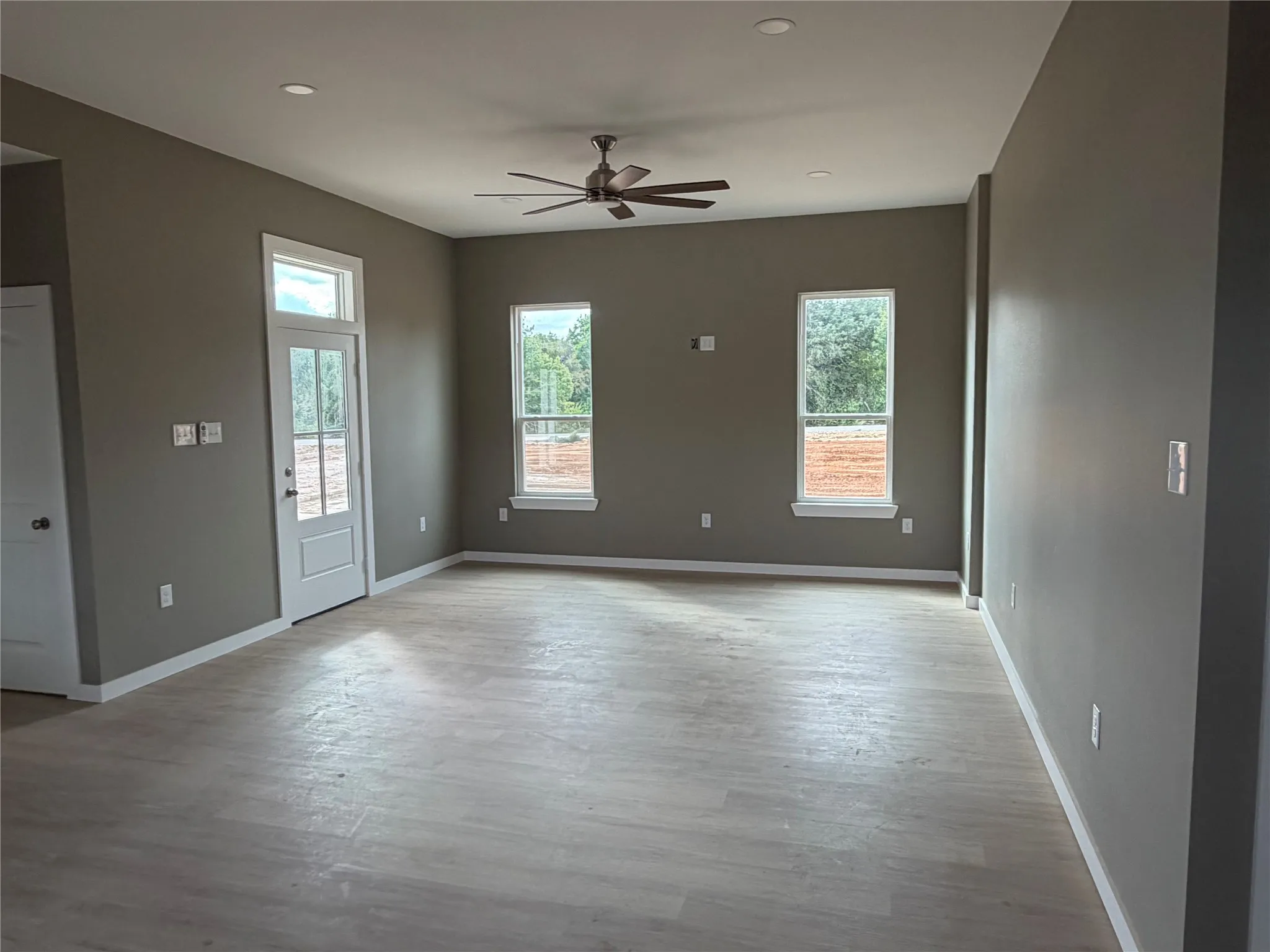 Neutral-toned interior featuring wood-finish flooring, recessed lighting, a modern ceiling fan, and large windows