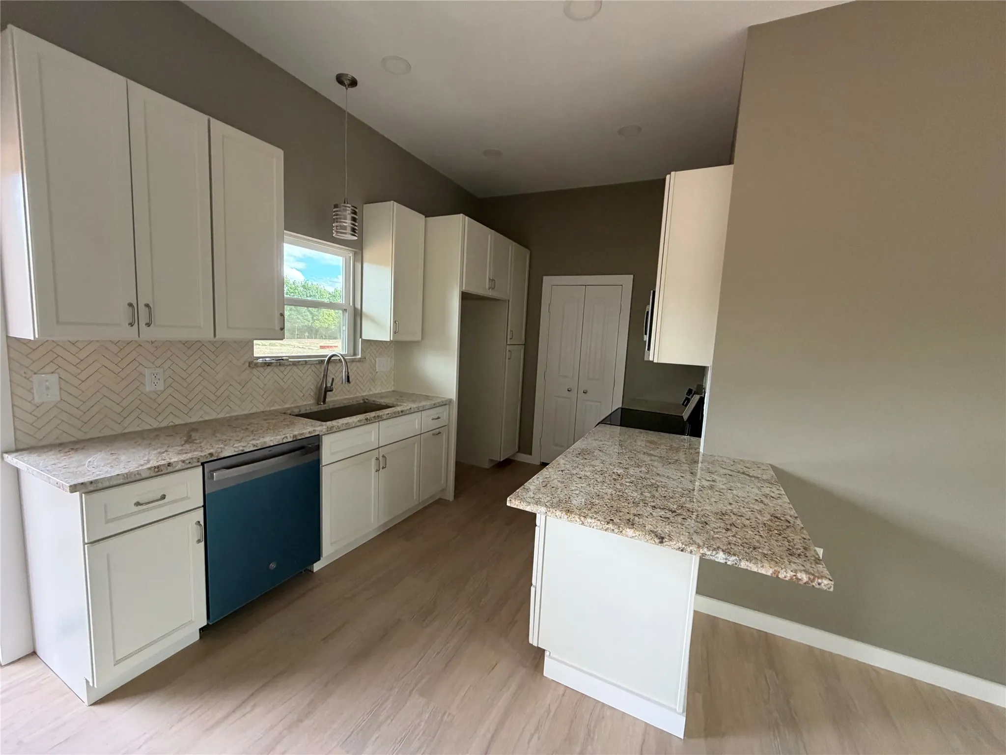 Kitchen featuring white cabinetry, stone-finish countertops, herringbone-patterned tile backsplash, peninsula counter, and wood-finish flooring