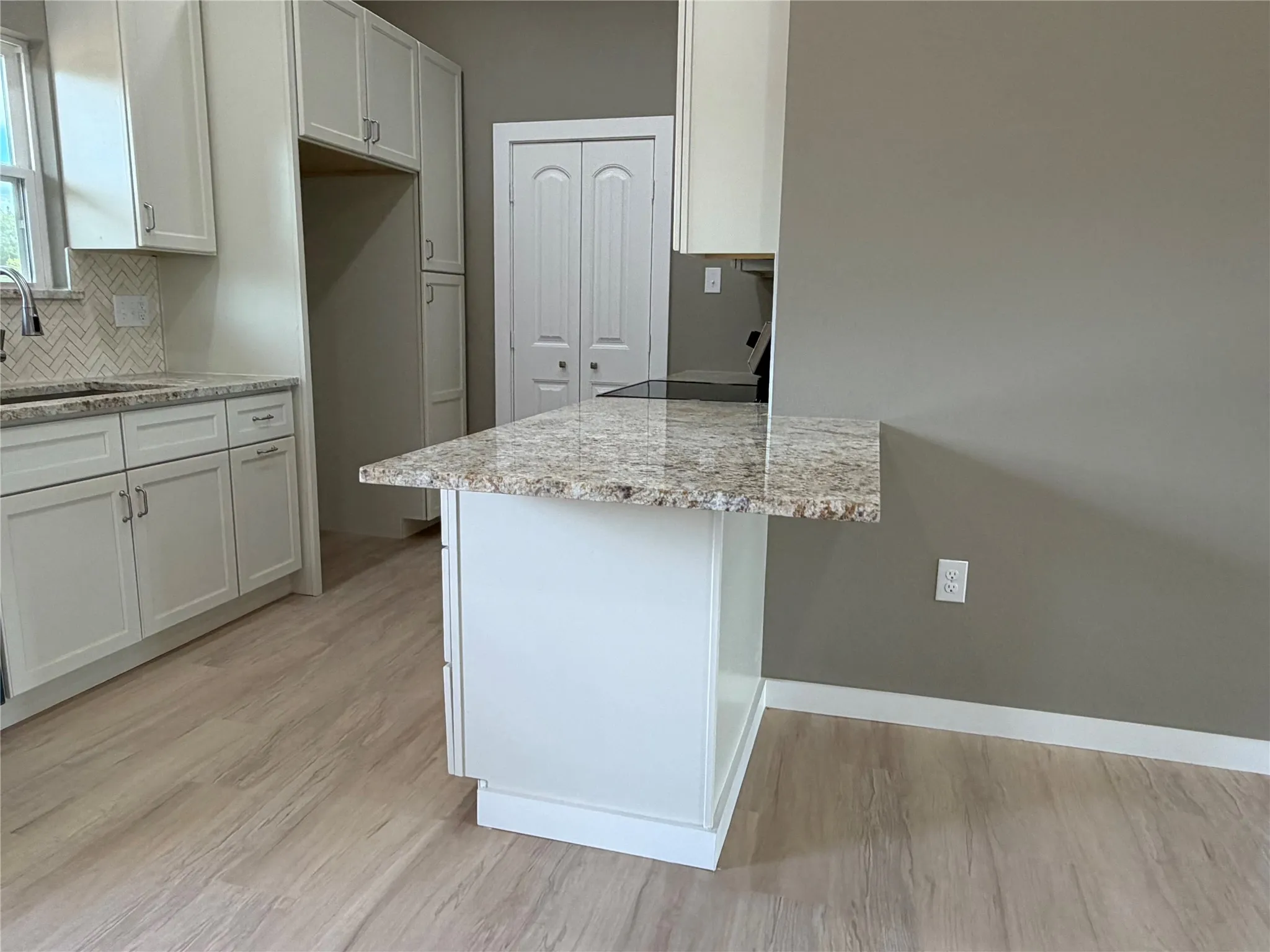 Kitchen featuring stone countertops, white shaker-style cabinetry, wood-finish flooring, a herringbone-patterned backsplash, and a breakfast bar peninsula
