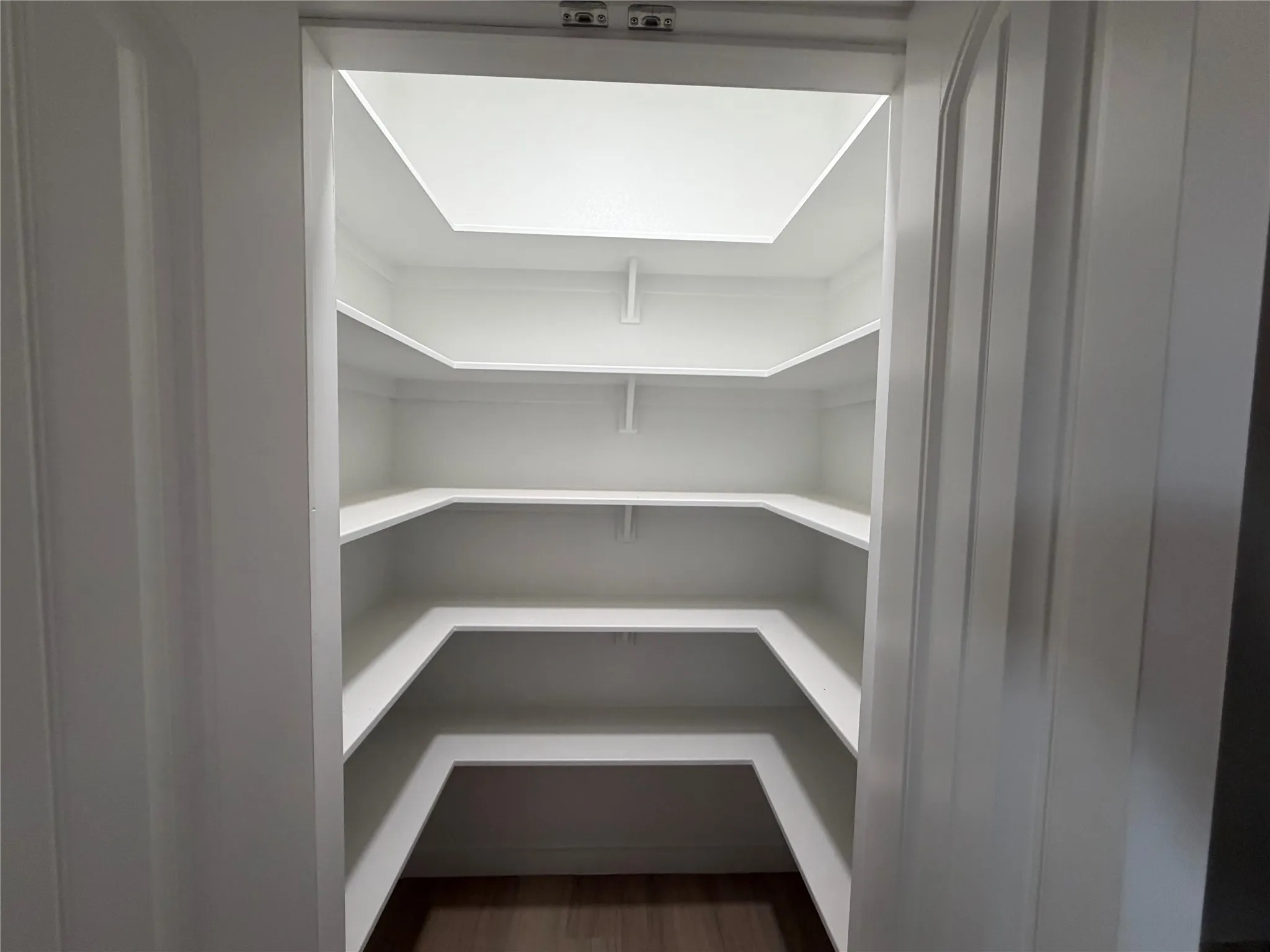 Storage space featuring three tiers of built-in shelving, a recessed ceiling light, and wood-finish flooring