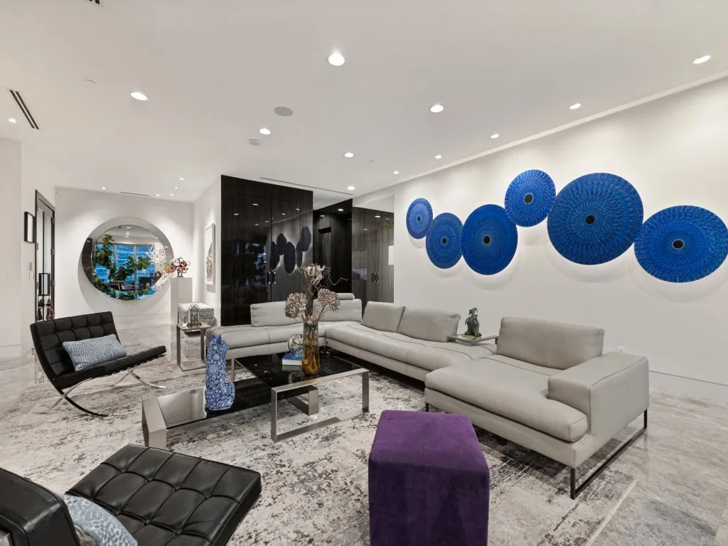 Recessed lighting illuminates the expansive living area with high ceilings, featuring a large circular wall mirror and dark wood-finish paneling