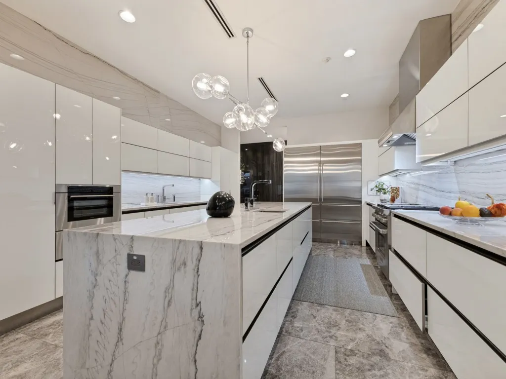 Integrated stainless steel appliances, marble-clad waterfall island, polished white cabinetry, contemporary chandelier, and recessed lighting
