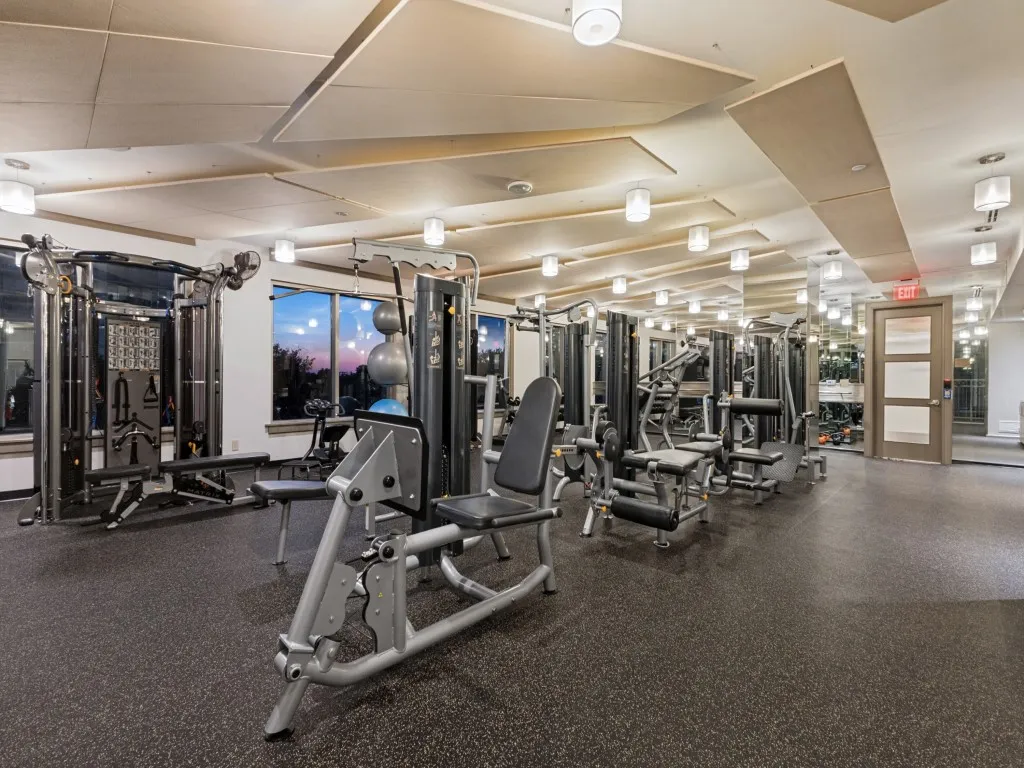 Fitness center with extensive exercise equipment, resilient flooring, large windows, and contemporary ceiling light fixtures